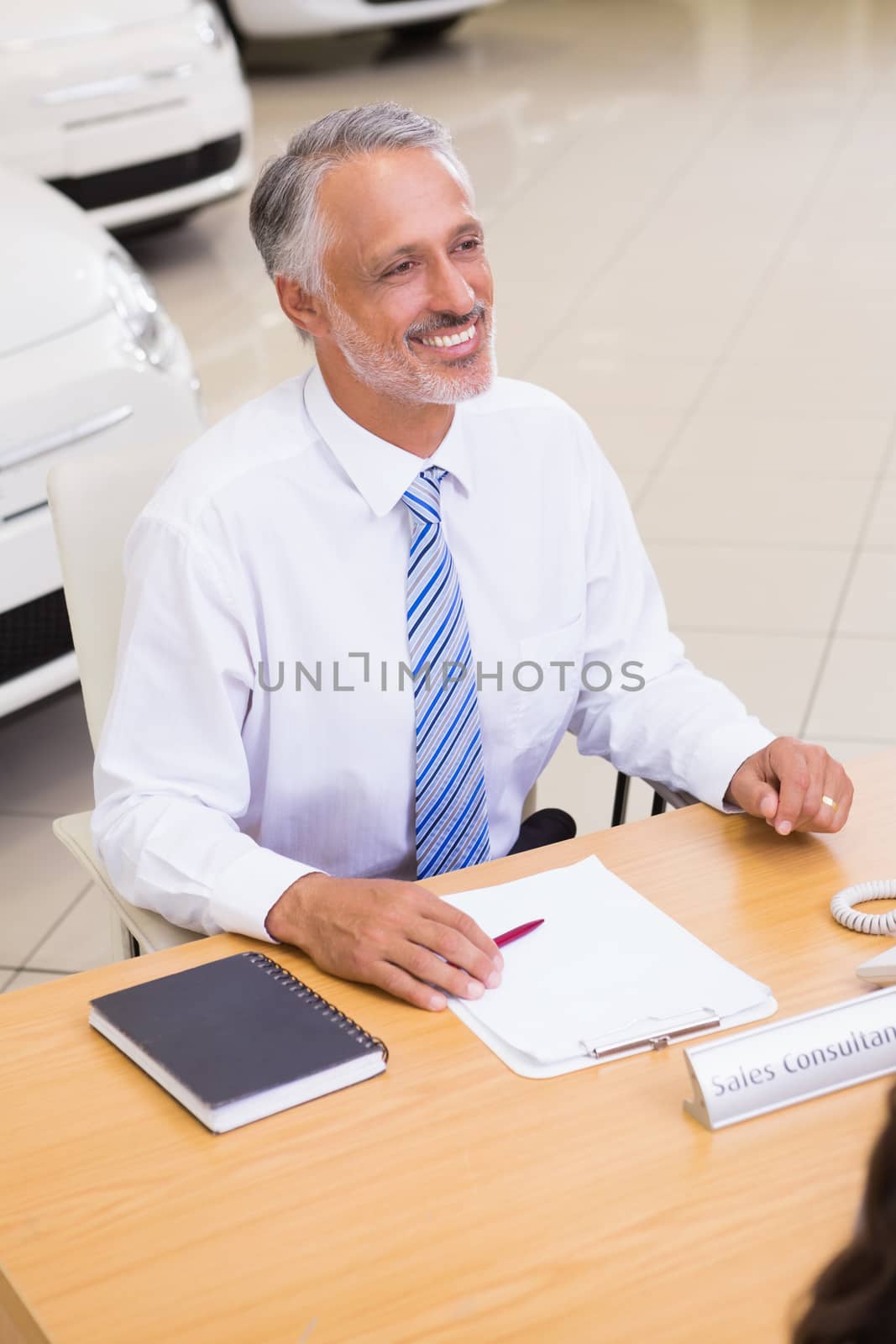 Happy businessman working at his desk at new car showroom