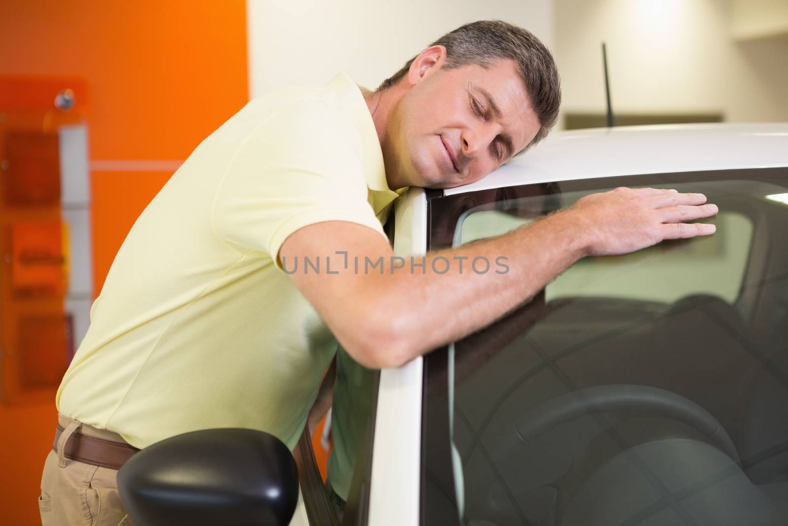 Smiling man hugging a white car at new car showroom