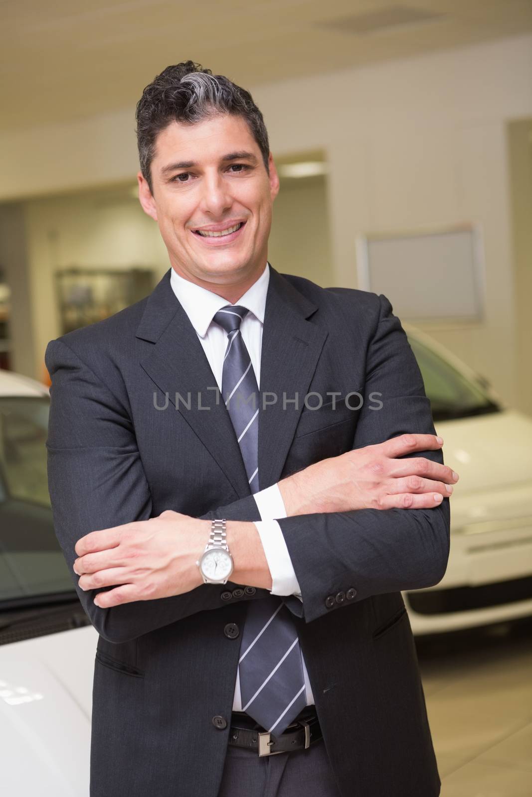 Smiling businessman standing with arms crossed at new car showroom