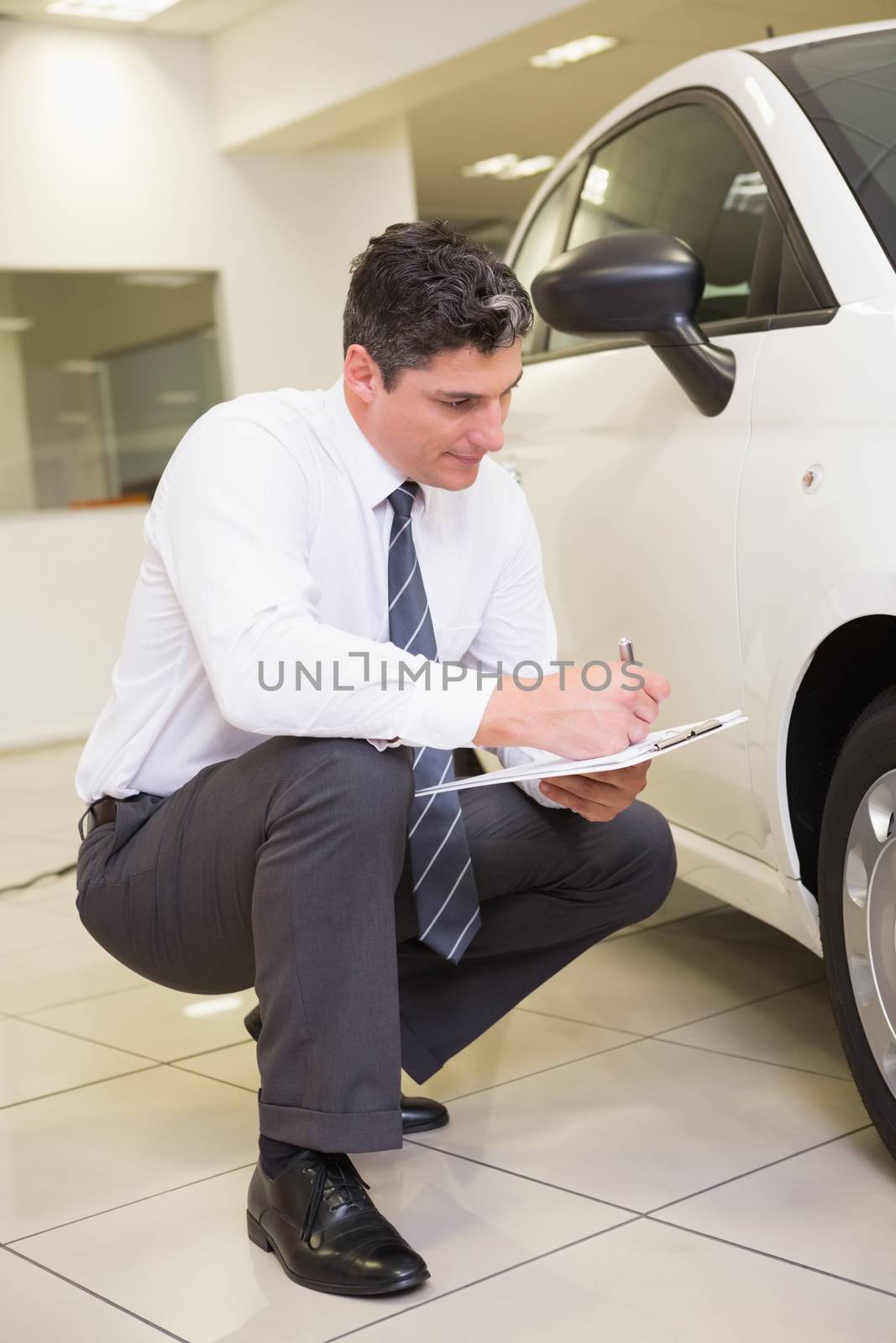 Businessman looking at car while writing on clipboard at new car showroom