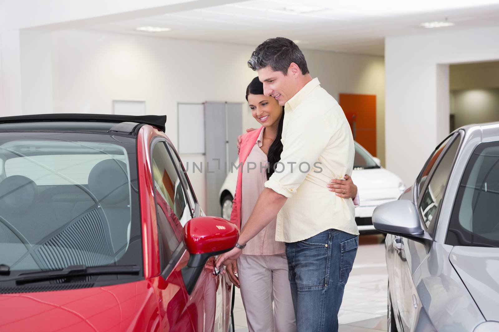 Couple talking together while looking at car at new car showroom