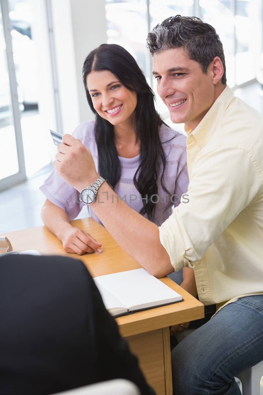 Smiling couple holding credit card to buy a car at new car showroom