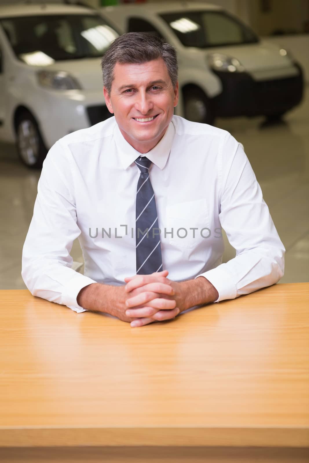 Happy businessman sitting at his desk at new car showroom