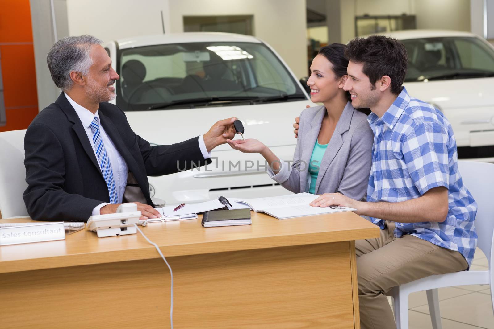 Salesman giving car keys to a couple at new car showroom