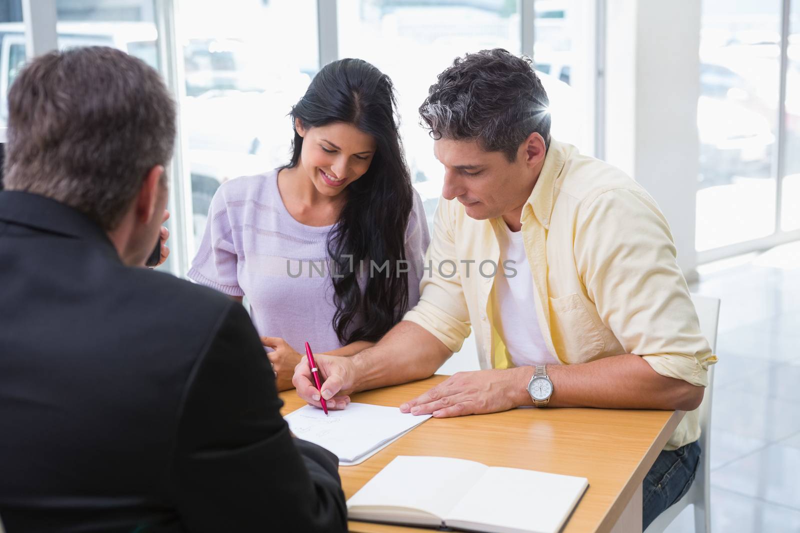 Smiling couple signing a contract at new car showroom