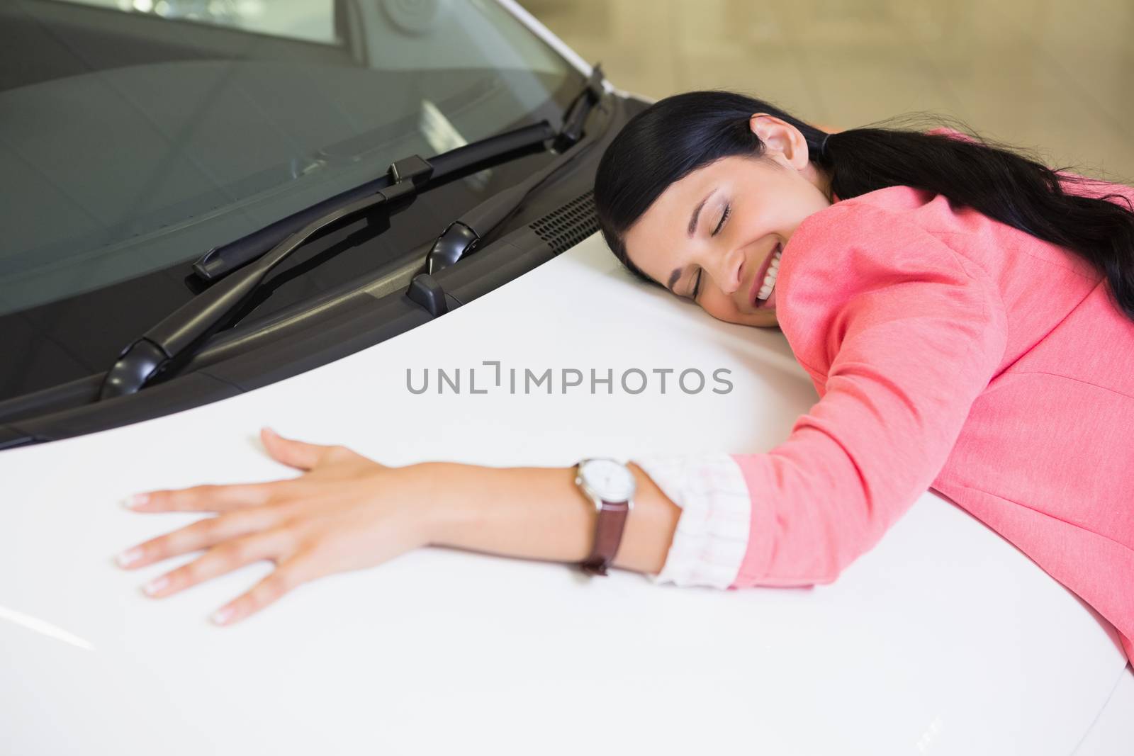 Smiling woman hugging a white car at new car showroom
