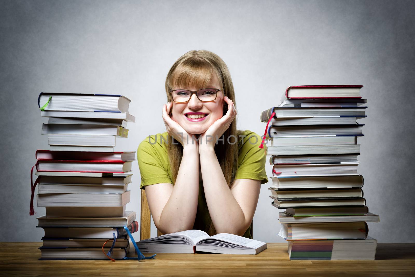 young happy female student with glasses and lots of books at a table