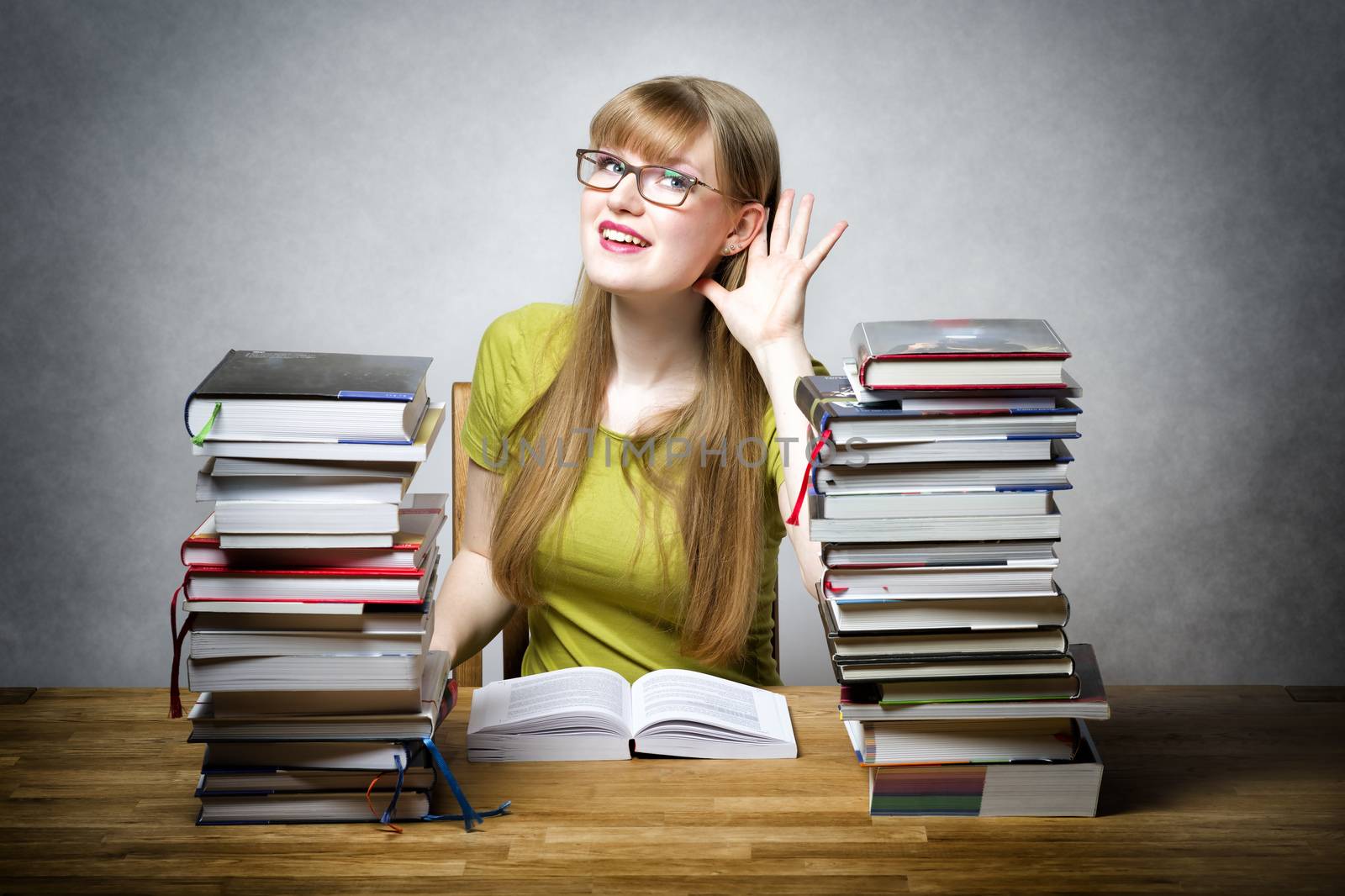 Happy female student with glasses and lots of books at a table is listening