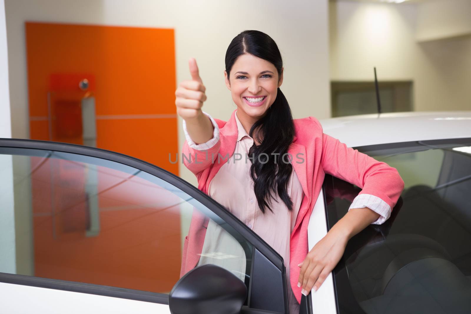Smiling customer leaning on car while giving thumbs up at new car showroom