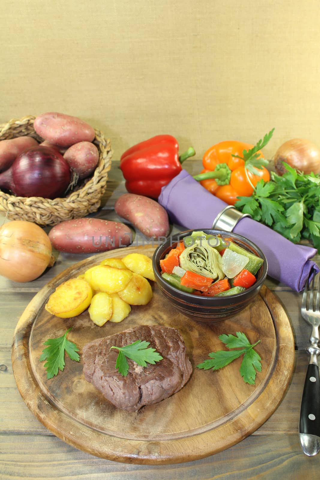 roasted ostrich steaks with baked potatoes and vegetables on a wooden board