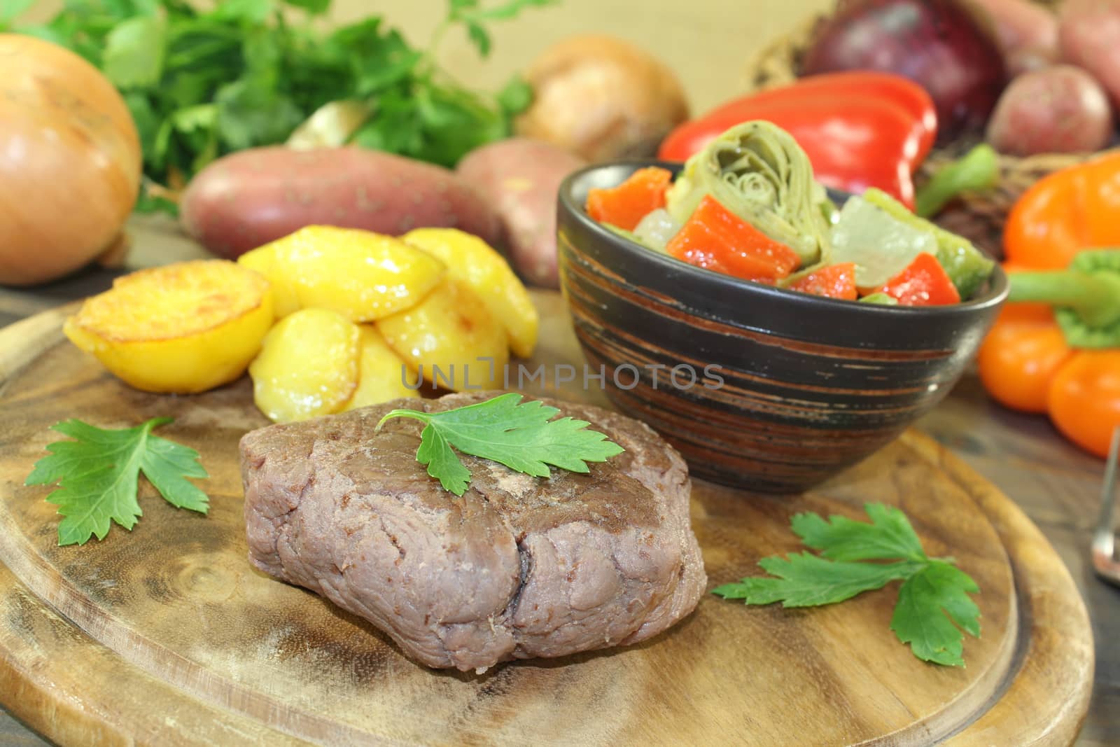 Ostrich steak with crispy baked potatoes and vegetables on a wooden board