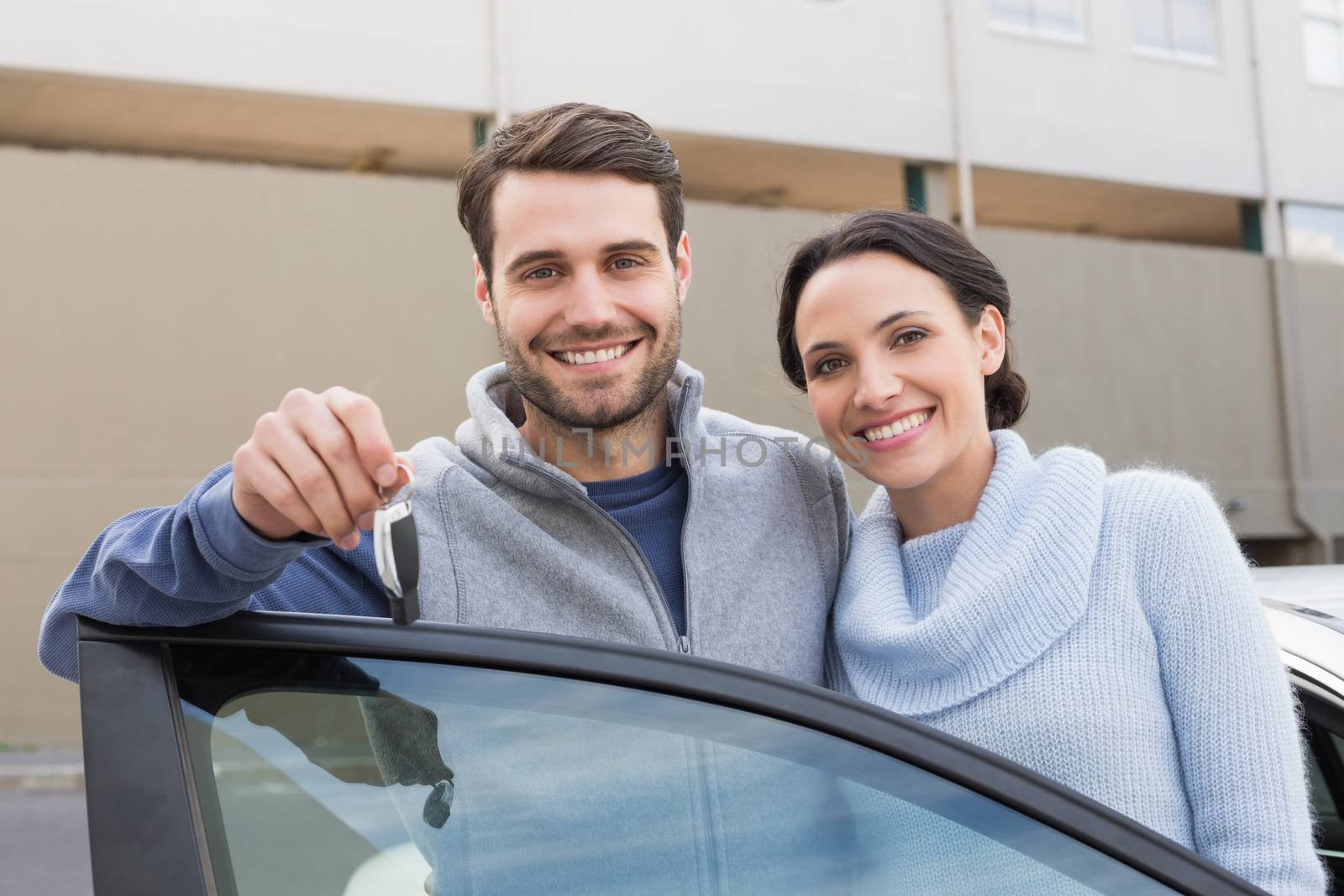 Young couple smiling holding new key outside their car