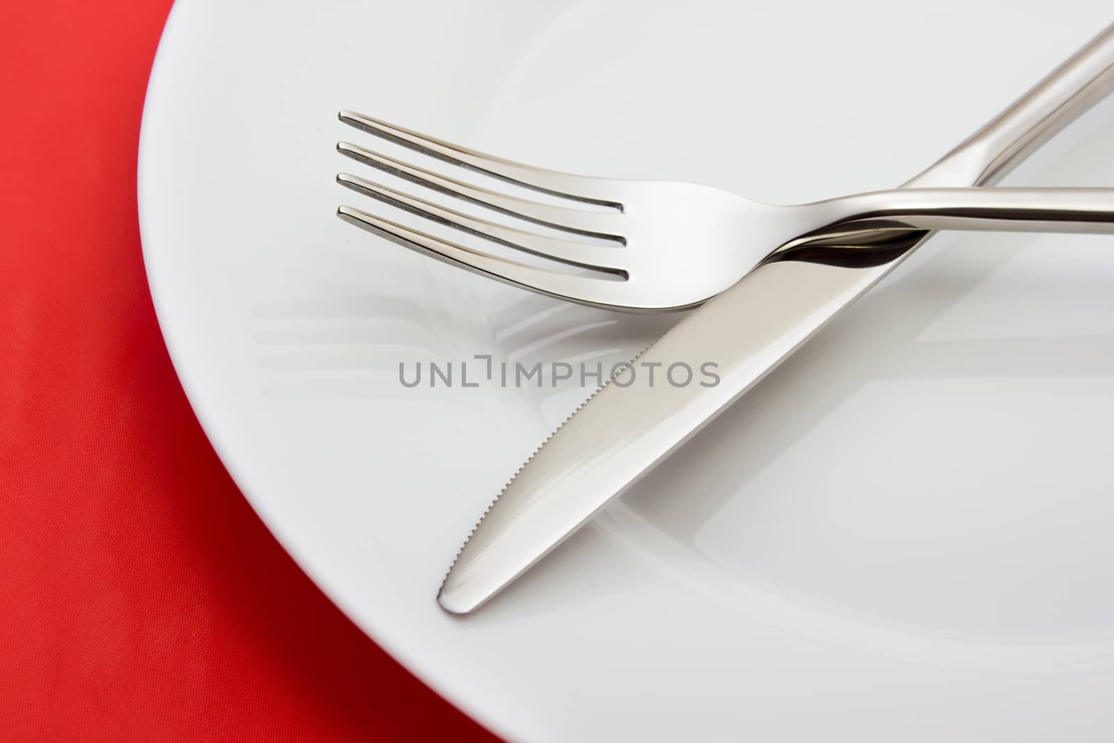 White empty plate with fork and knife on red