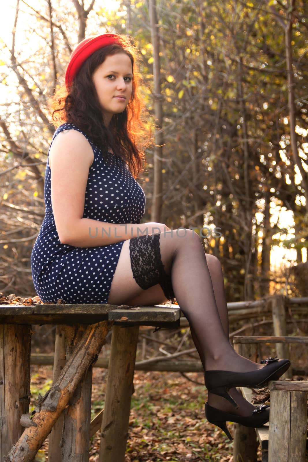 Young girl sitting on a table in a dress and hat in nature