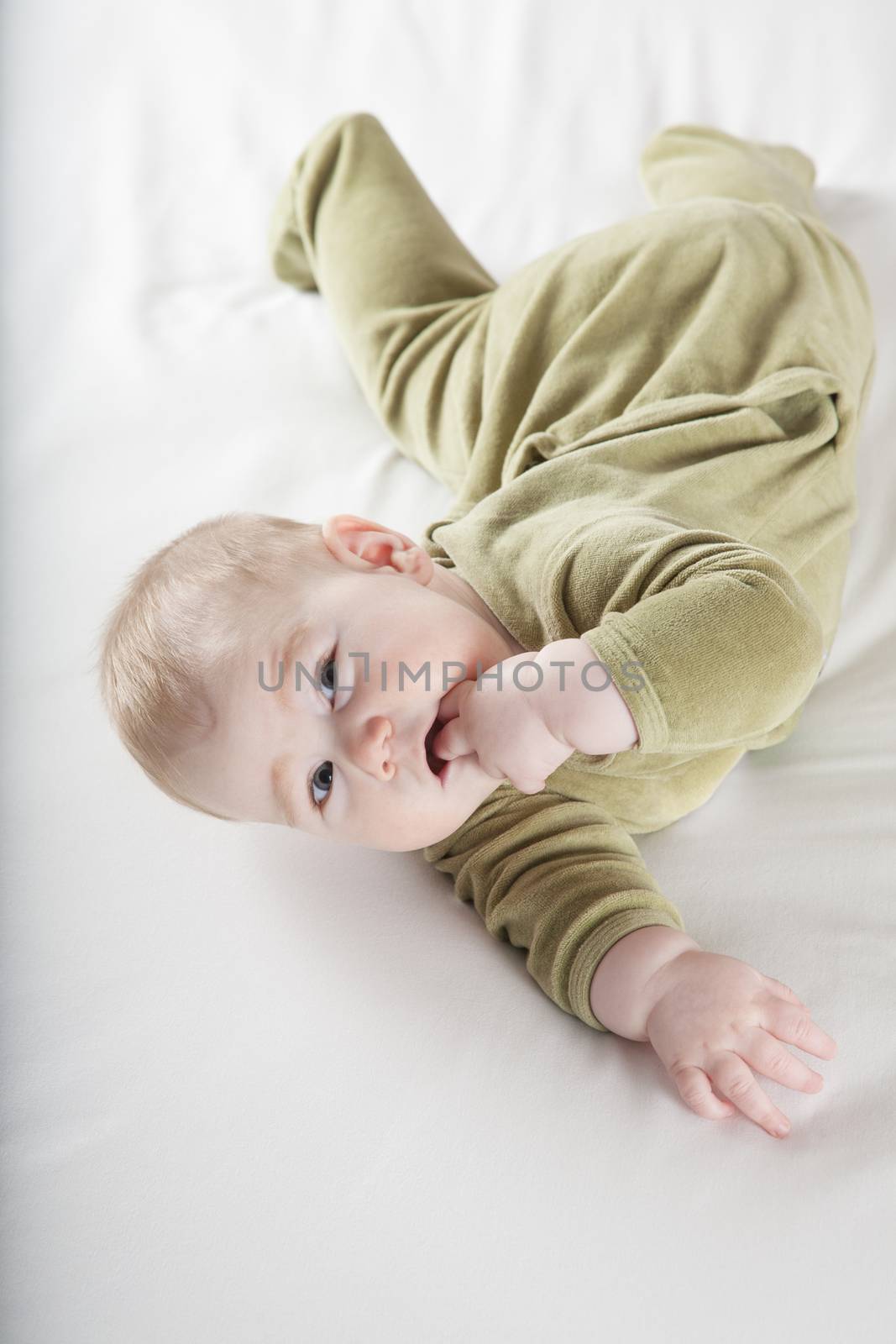 six months age blonde baby green velvet onesie lying on white sheet bed smiling happy face