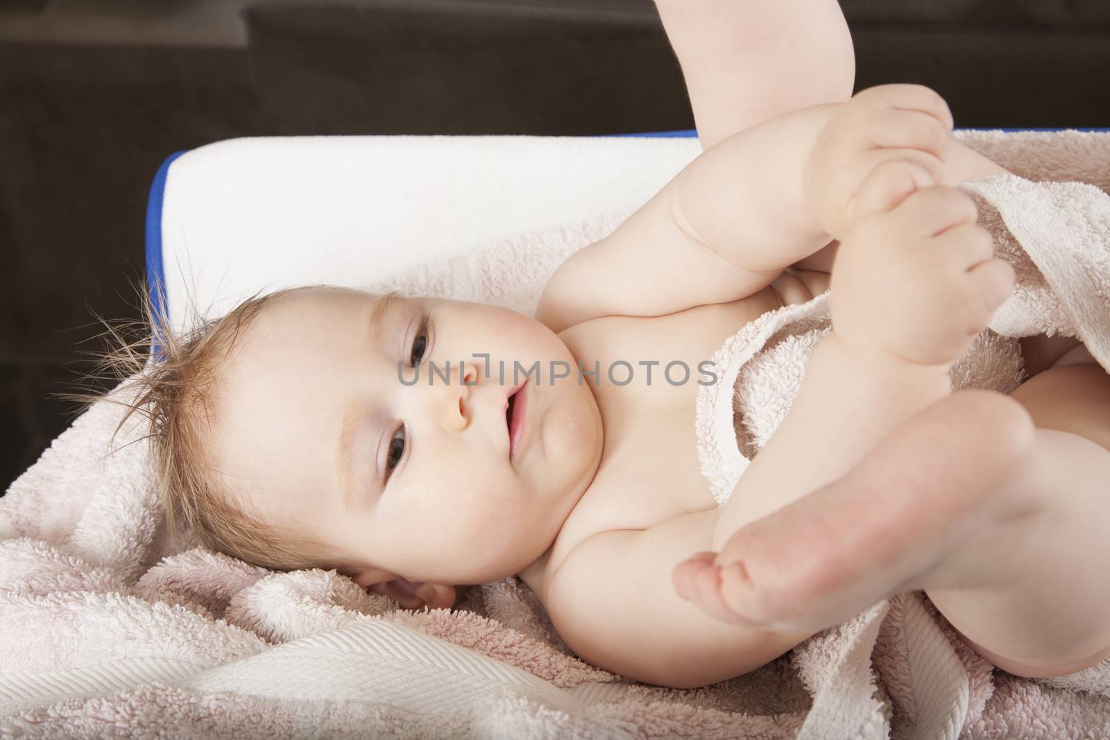 portrait of eight months age blonde lovely cute baby face wet hair with legs up lying on towel
