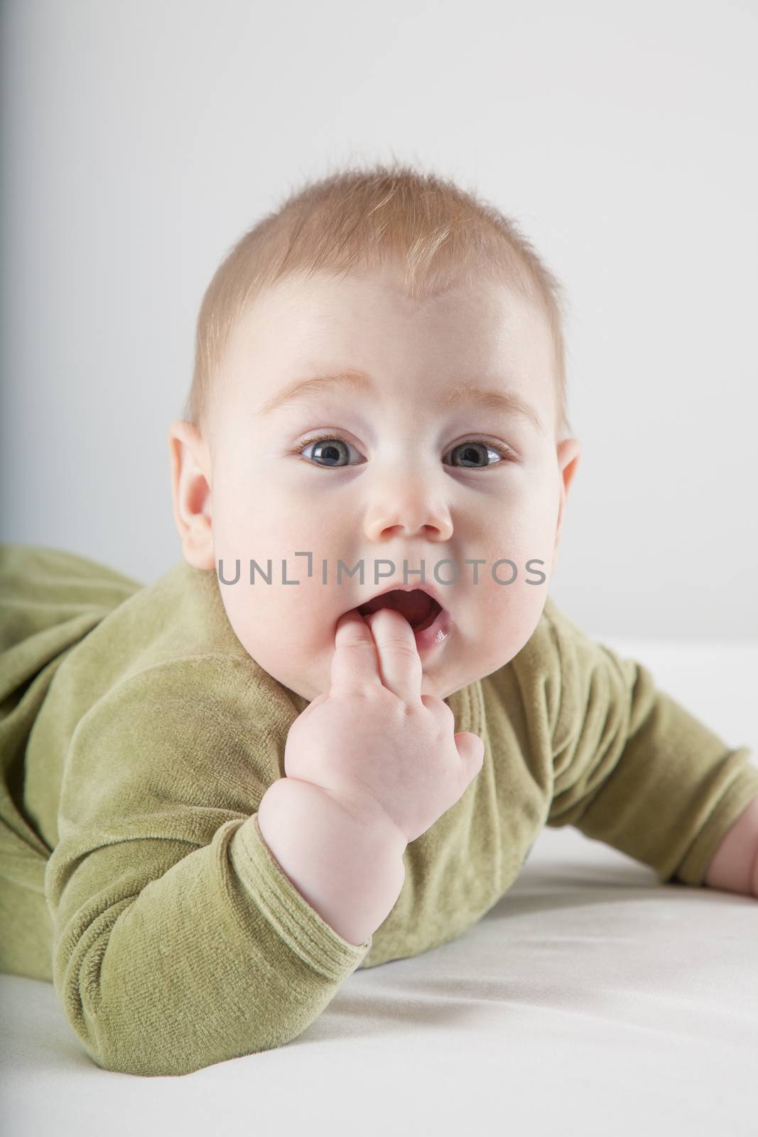 six months age blonde baby green velvet onesie lying on white sheet bed smiling happy face