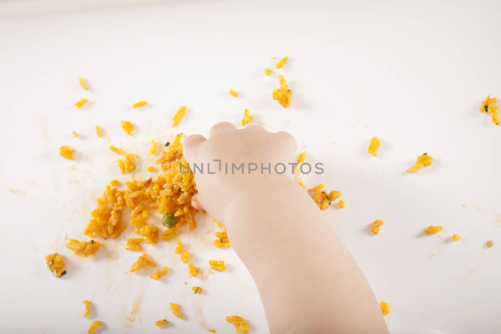 overhead shot of one year age caucasian baby hand taking yellow rice on white table