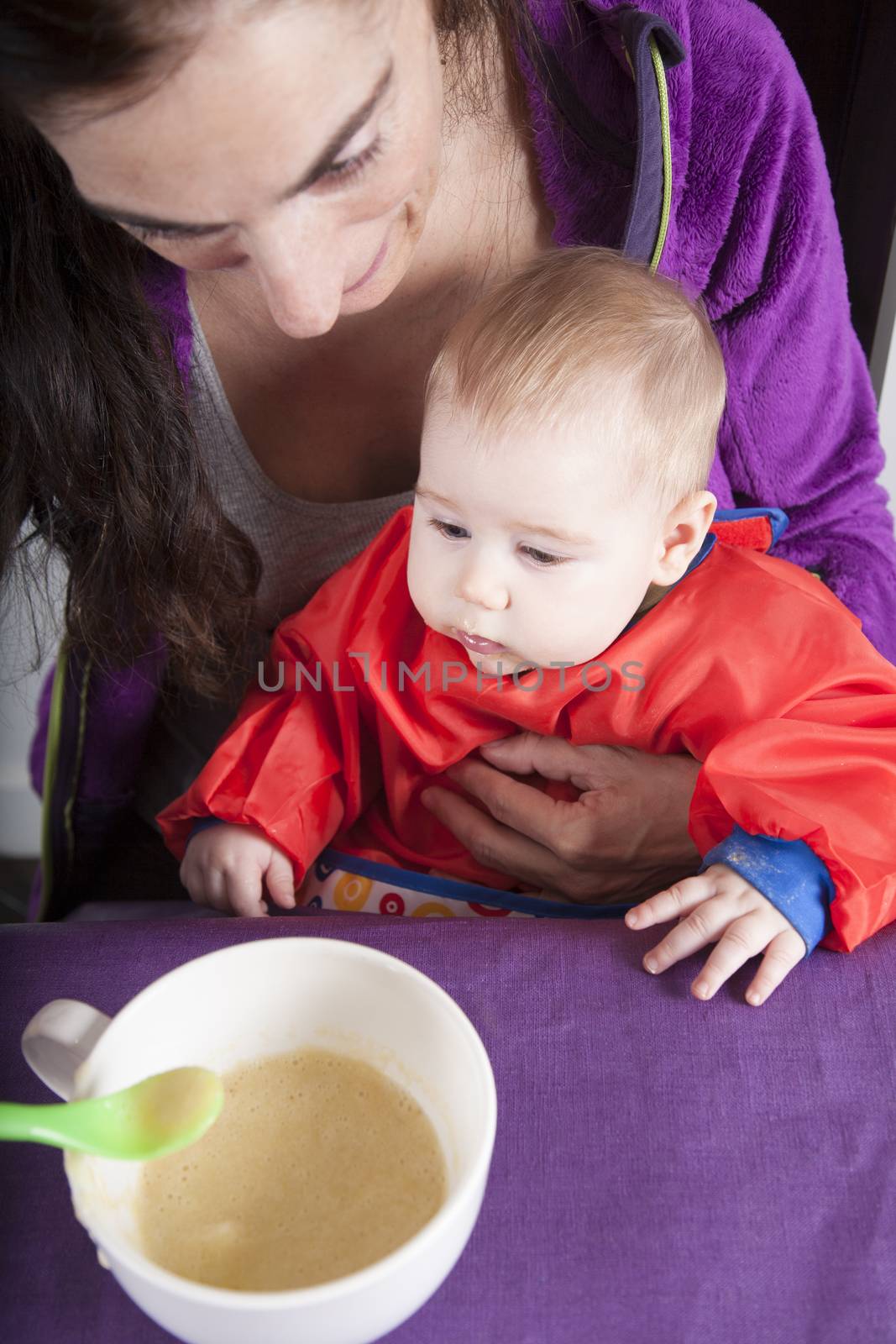 six months age blonde caucasian baby red bib in woman mother purple velvet jacket arms eating puree