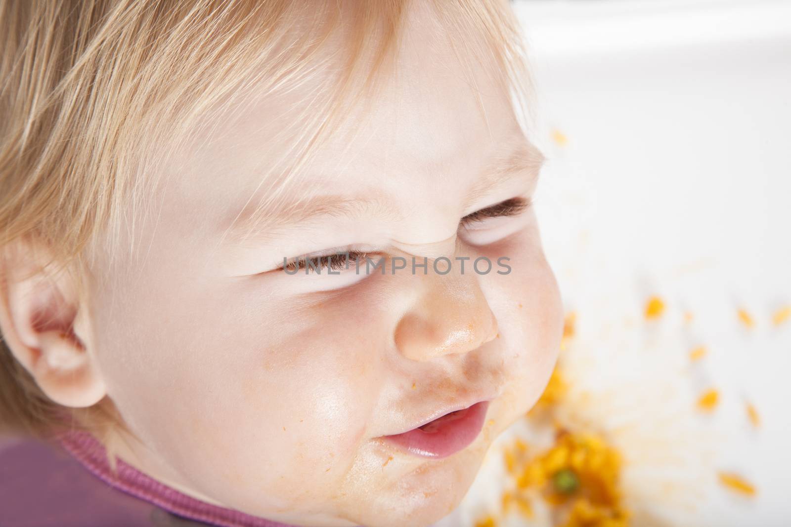 overhead shot of one year age caucasian baby pink plastic bib eating meal yellow orange rice paella with her hand in white high-chair