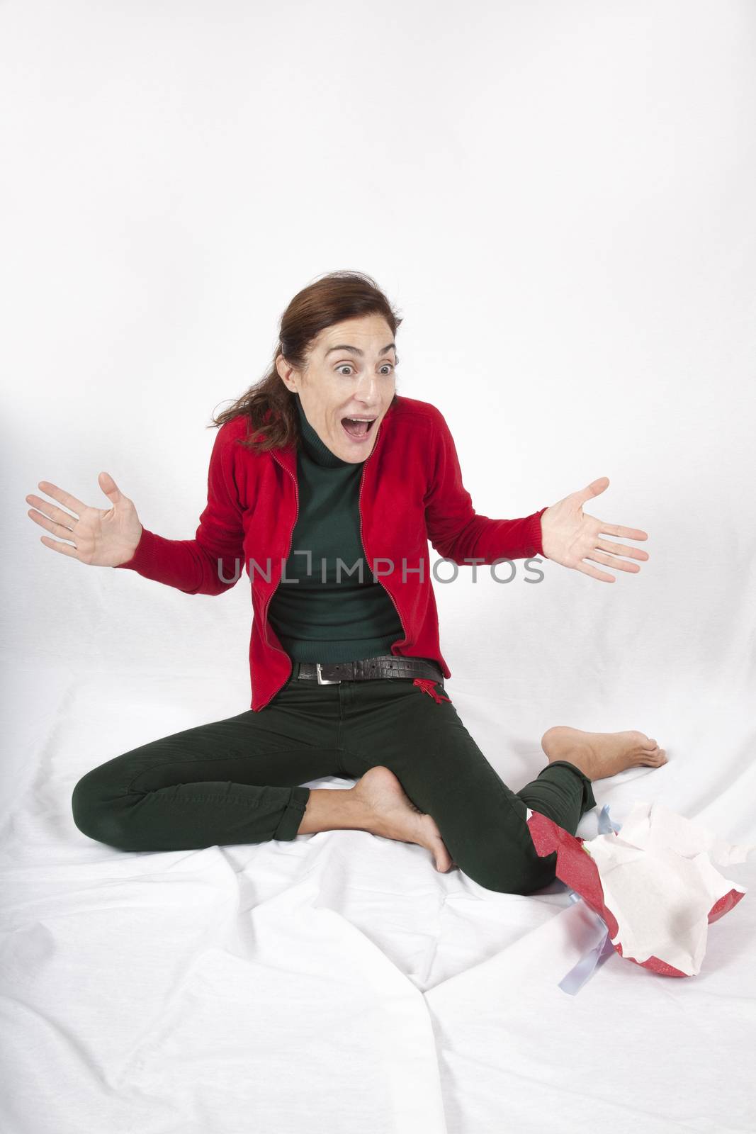 brunette caucasian woman red cardigan green trousers barefoot surprised looking open arms sitting on white background
