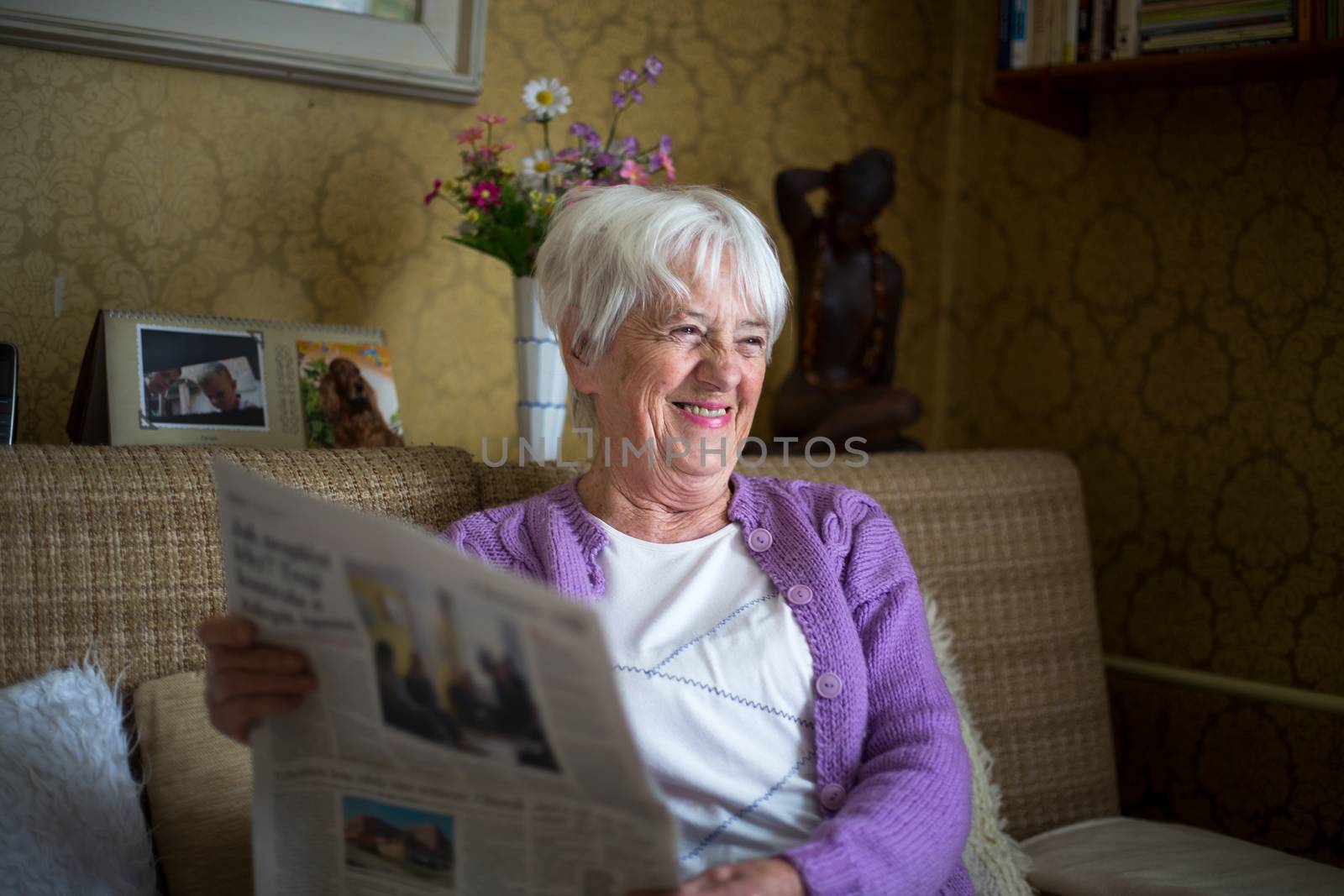 Senior woman reading morning newspaper, sitting in her favorite chair in her living room, looking happy