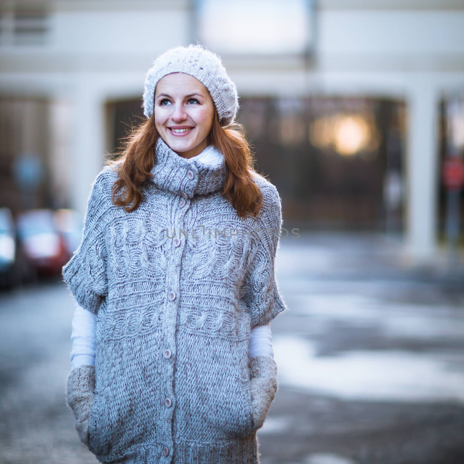 Autumn/winter portrait: young woman dressed in a warm woolen cardigan posing outside in a city park