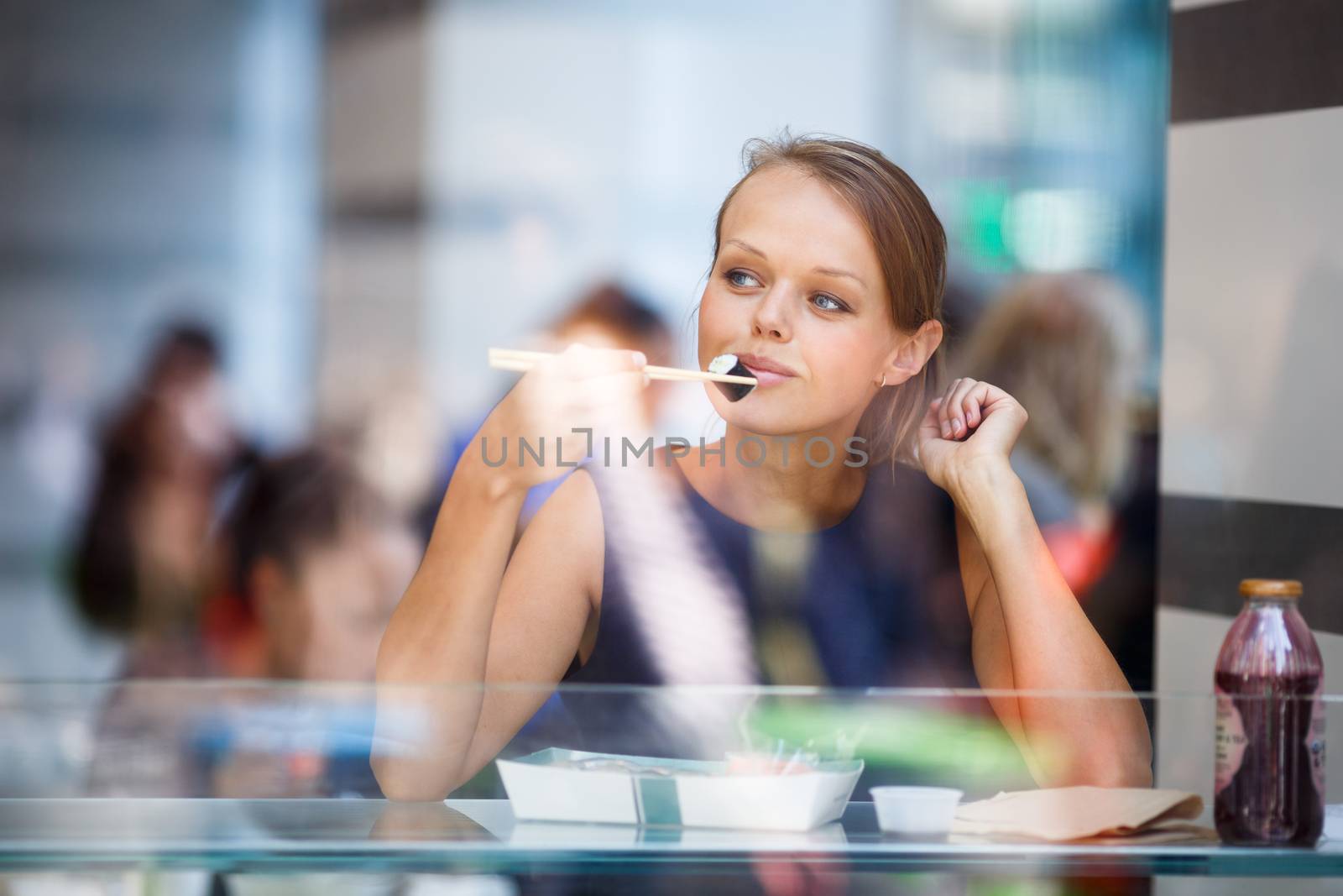 Pretty, young womna eating sushi in a restaurant, haivng her lunch break, enjoying the food, pausing for a while from her busy corporate/office life (color toned image)