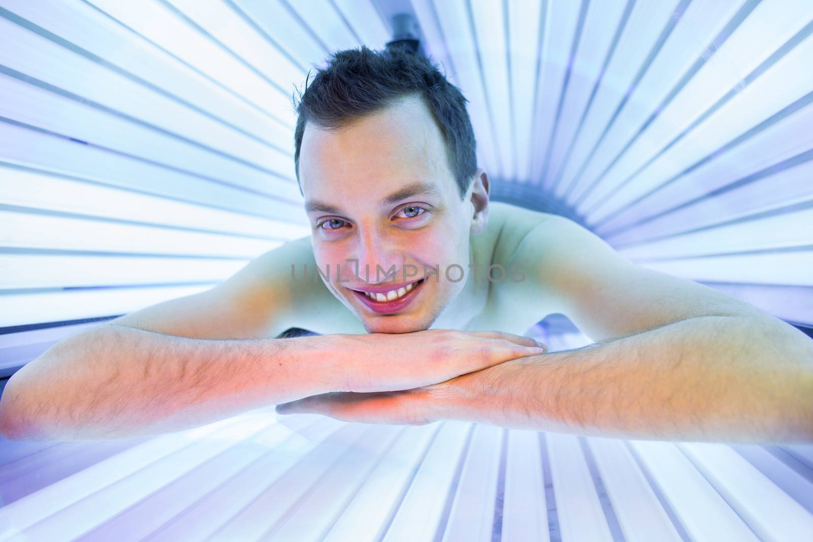 Handsome young man relaxing during a tanning session in a modern solarium, taking care of himself, enjoying the artificial sunlight.