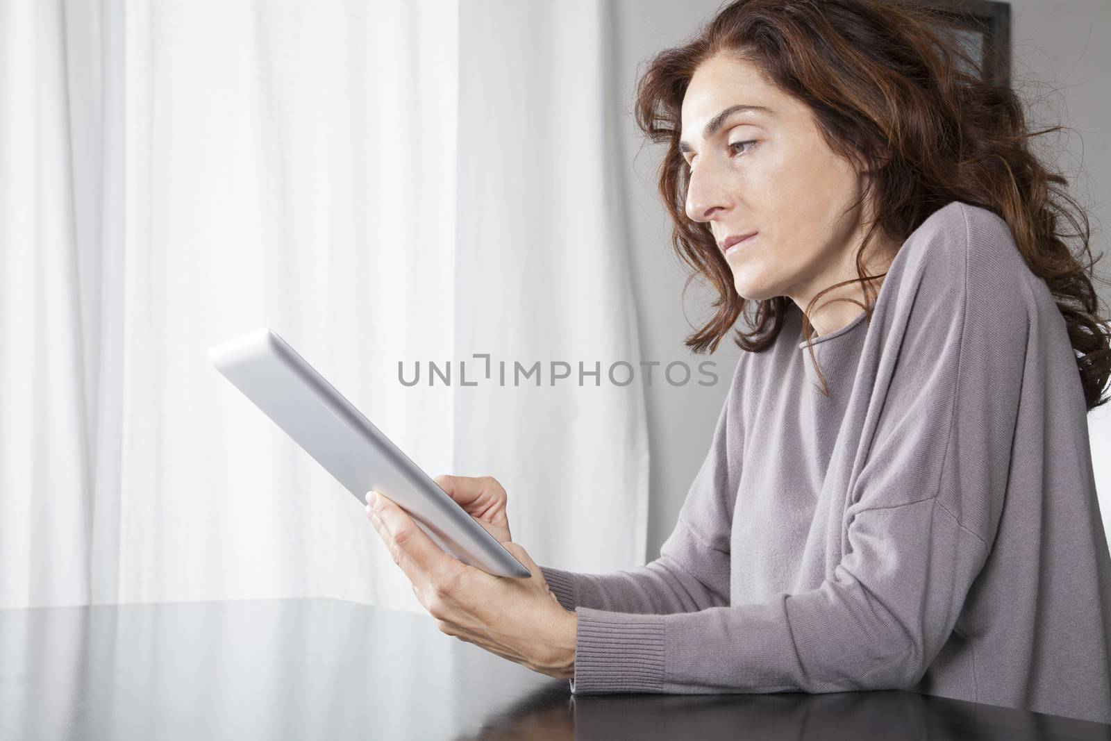 woman hand grey sweater finger touching digital tablet blank screen on black reflect table white curtain indoor