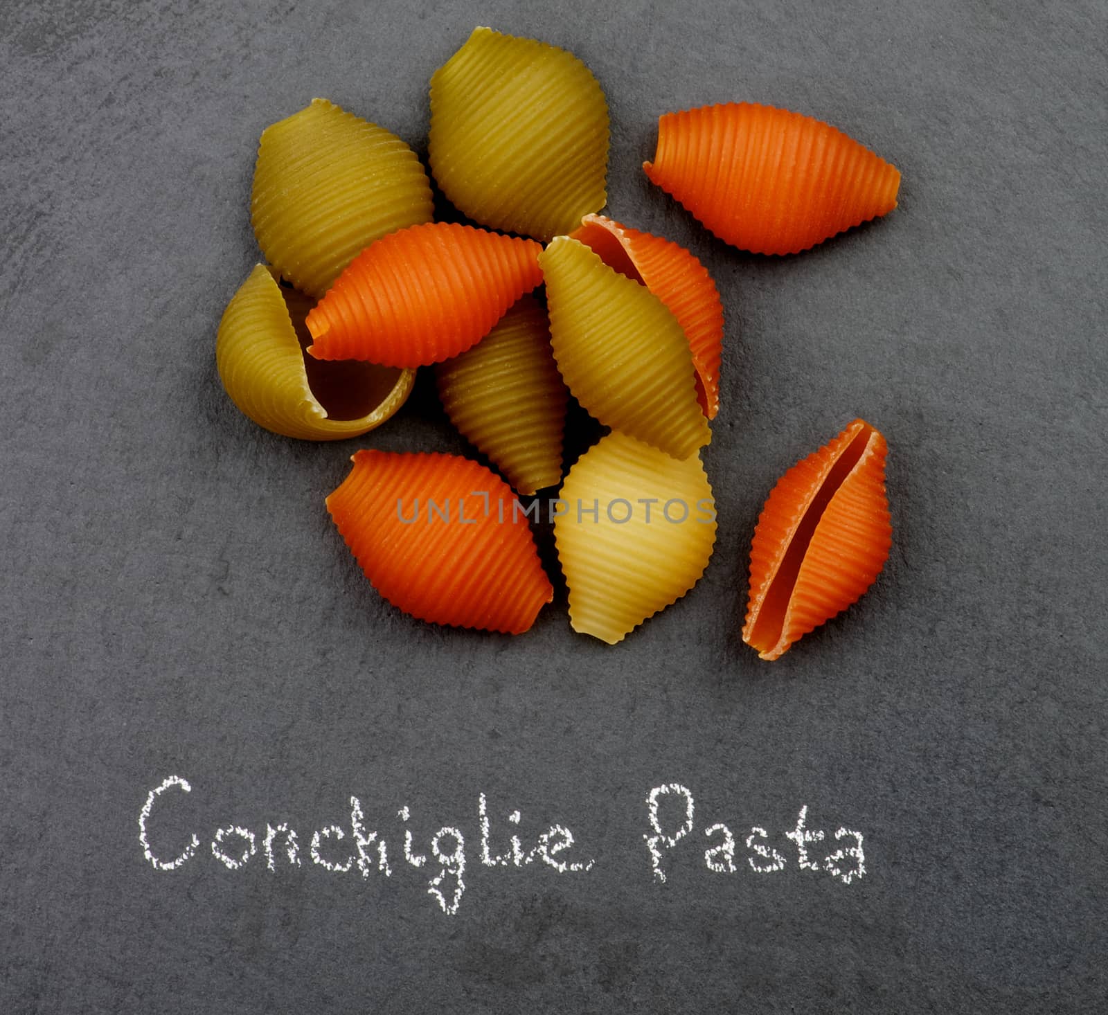 Heap of Raw Conchiglie Tricolore Pasta with Inscription closeup on Black Stone background