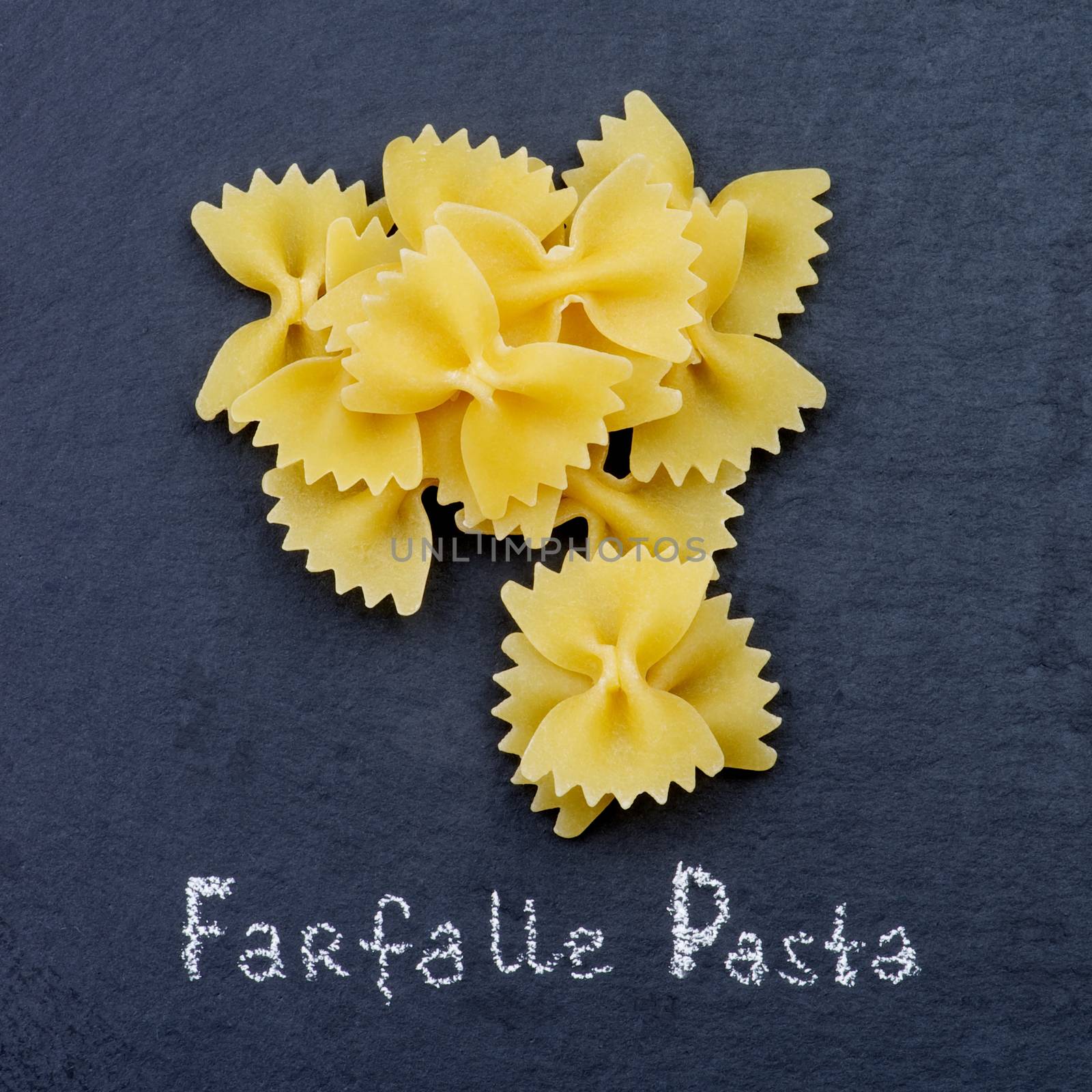 Heap of Raw Farfalle Pasta with Inscription closeup on Black Stone background