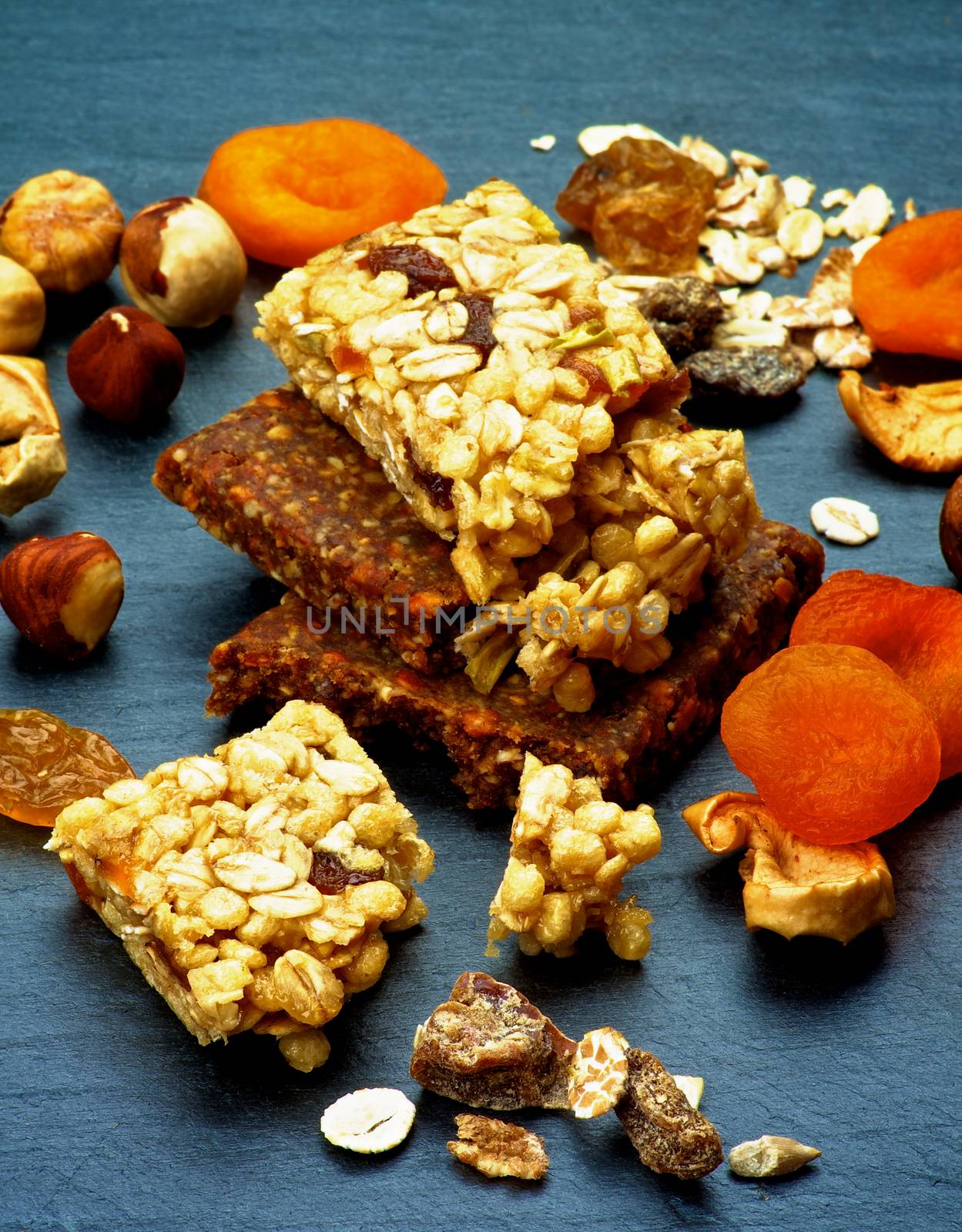 Stack of Useful Granola Bars with Muesli, Nuts, Seed, Raisins and Dried Apricots closeup on Black Stone background