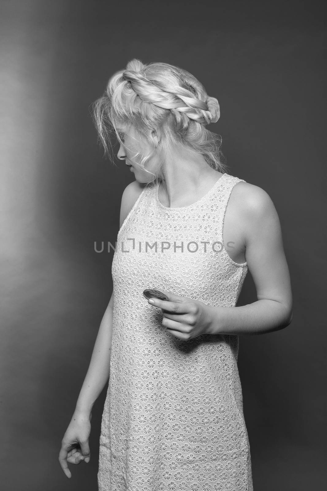 Blonde girl in mini dress made of lace and stylish hairstyle with biscuit in hand looks backwards. Black and white image, studio shot.