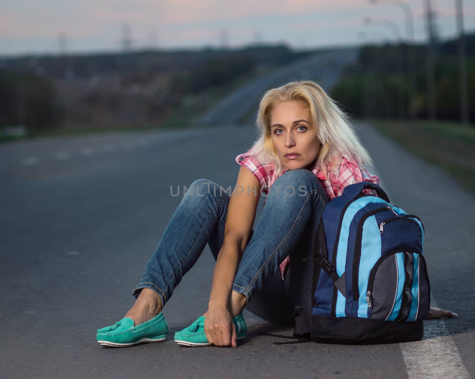 Woman with haversack sitting on the road by Valengilda