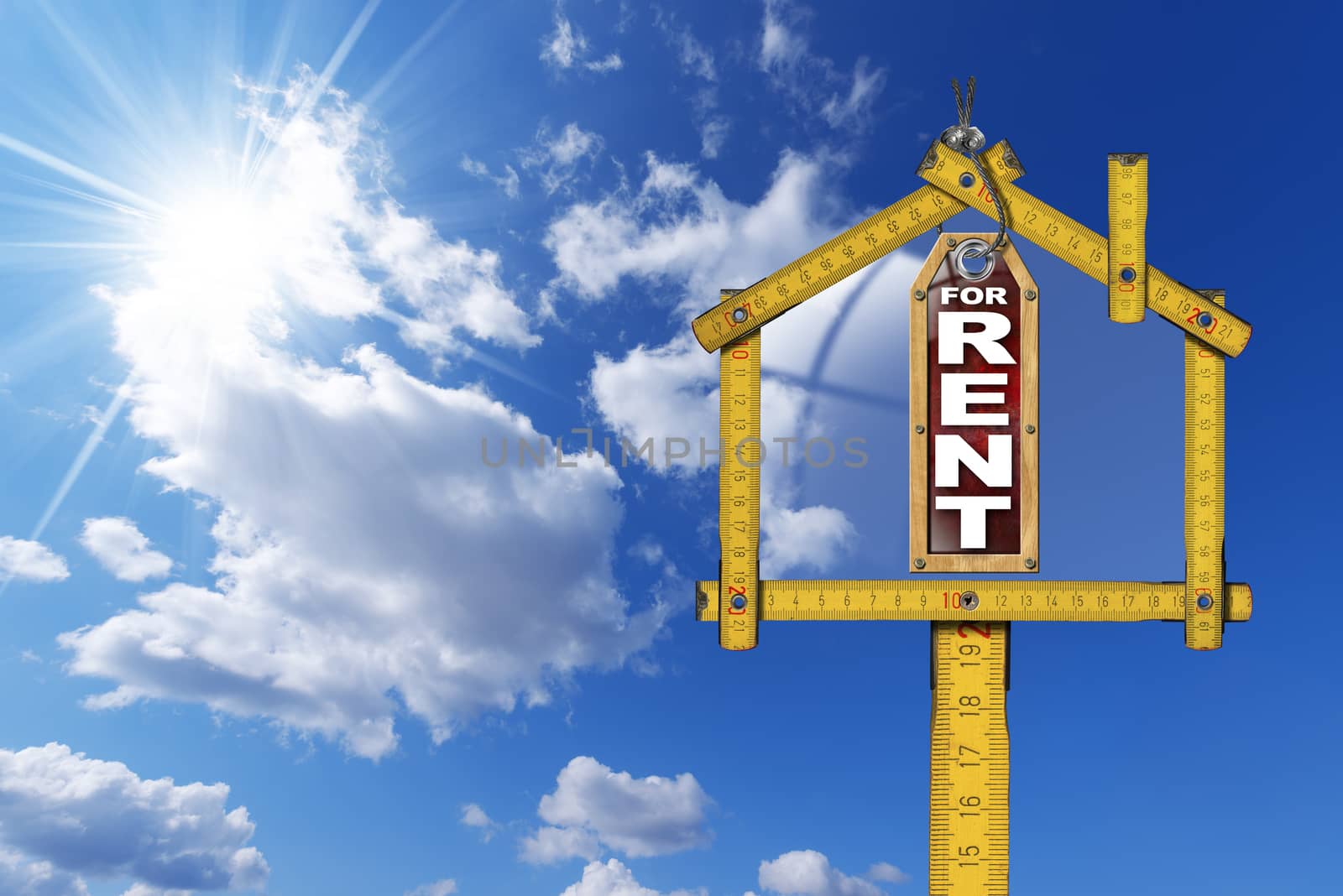 Yellow wooden meter ruler in the shape of house and label with text for rent. For rent real estate sign on blue sky with clouds and sun rays 