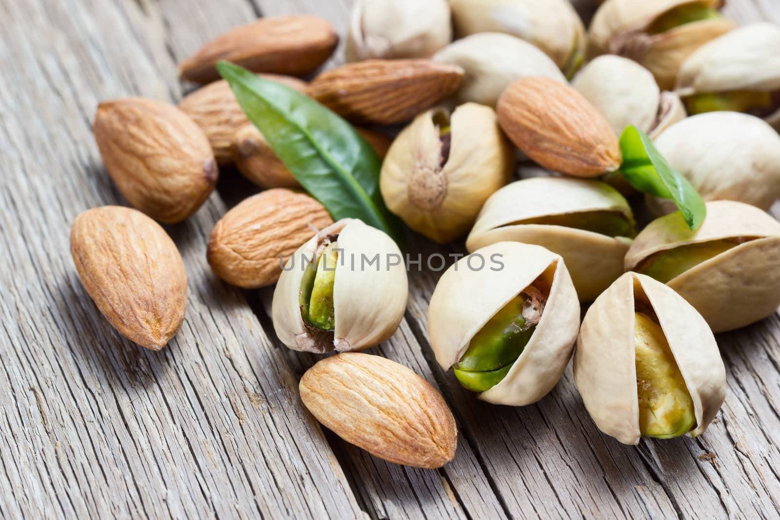 Almond and pistachio with leaves on wooden background