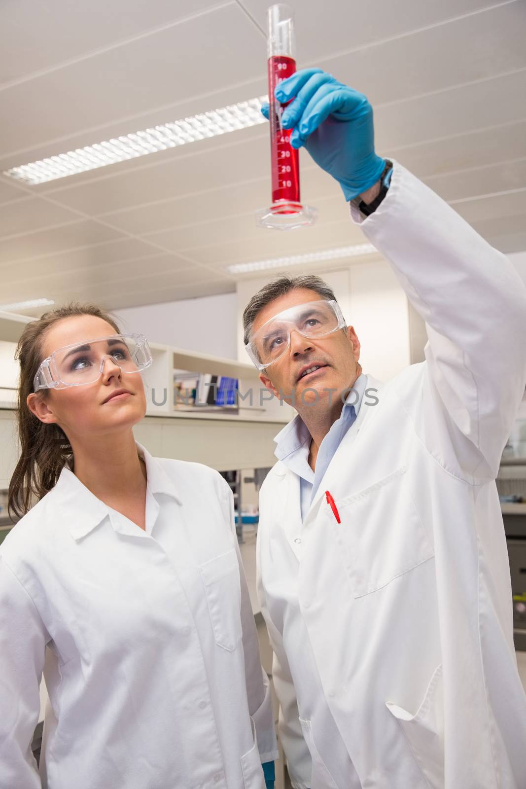 Pharmacists looking at beaker of red liquid at the laboratory