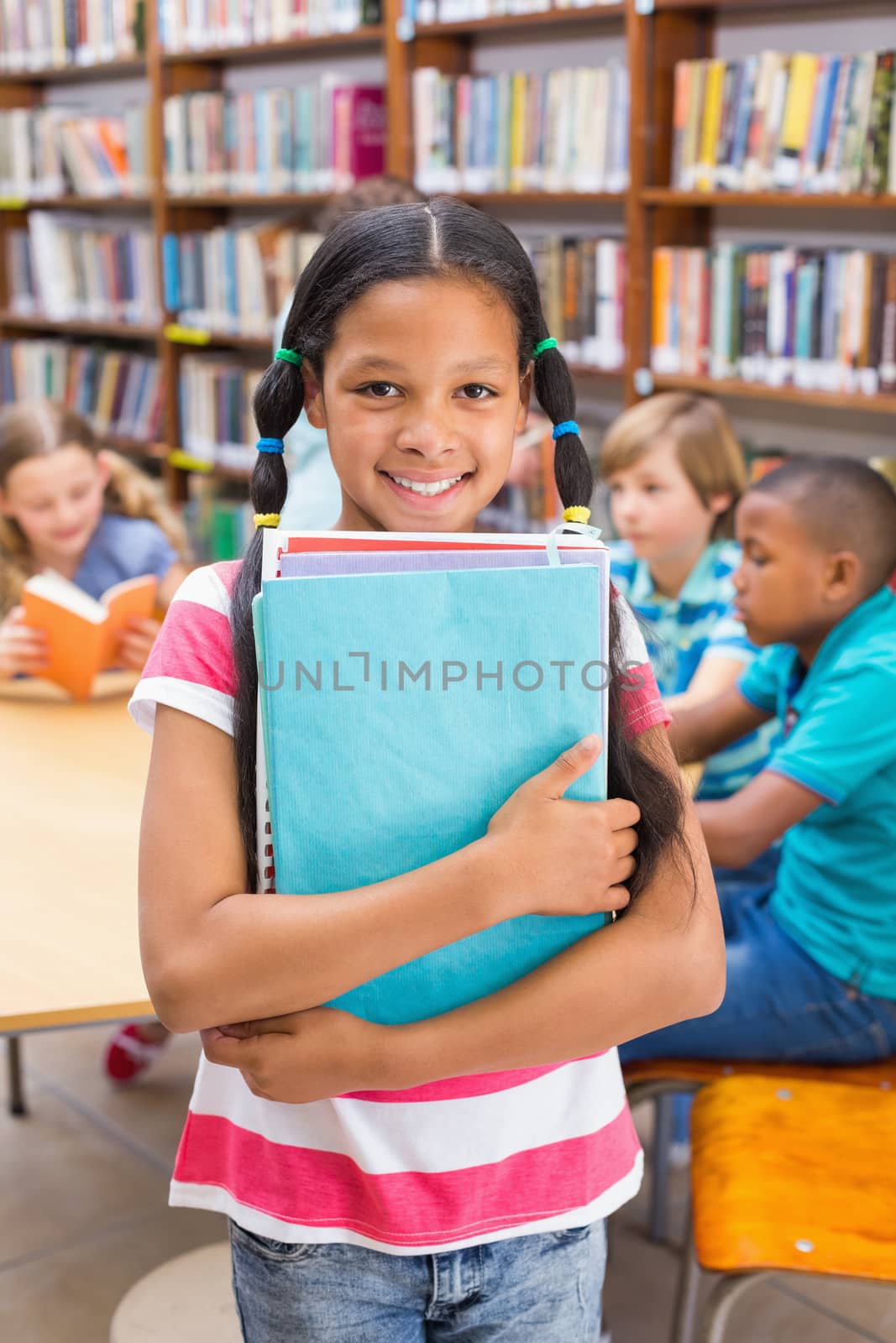 Cute pupil smiling at camera in library at the elementary school