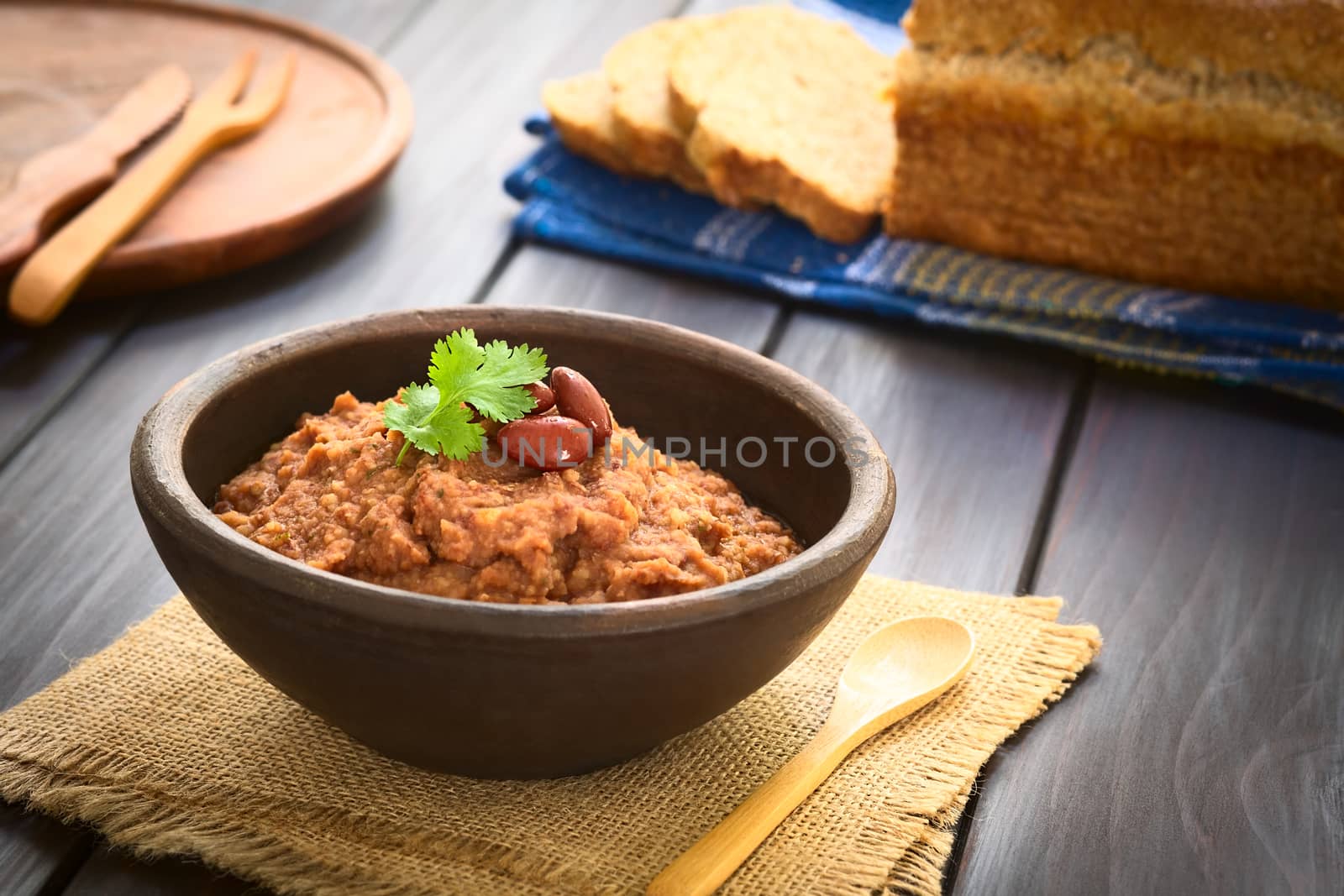 Rustic bowl of homemade red kidney bean spread garnished with kidney beans and fresh coriander leaf, wholegrain bread in the back, photographed with natural light (Selective Focus, Focus on the leaf) 