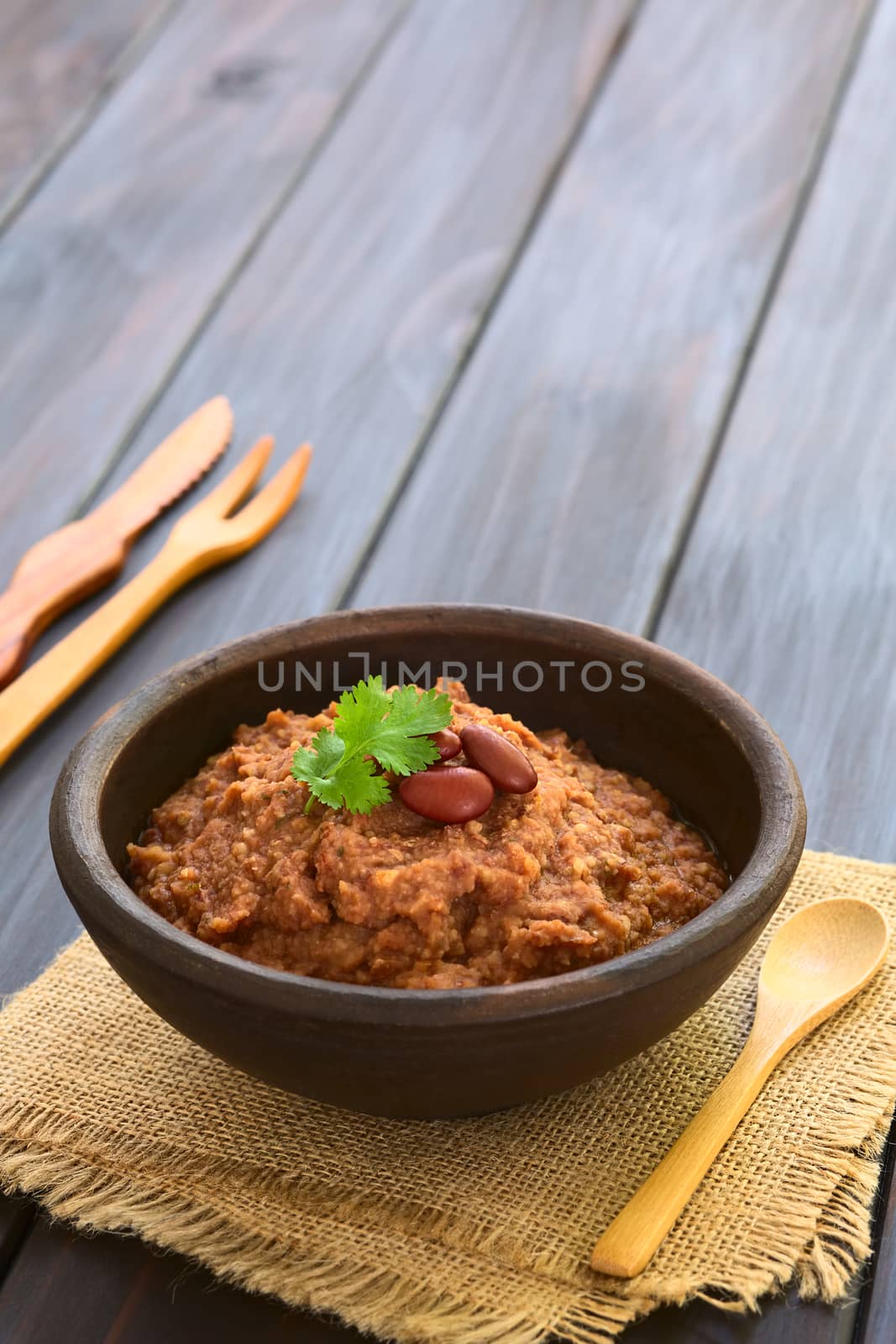 Rustic bowl of homemade red kidney bean spread garnished with kidney beans and fresh coriander leaf, photographed on dark wood with natural light (Selective Focus, Focus on the leaf) 