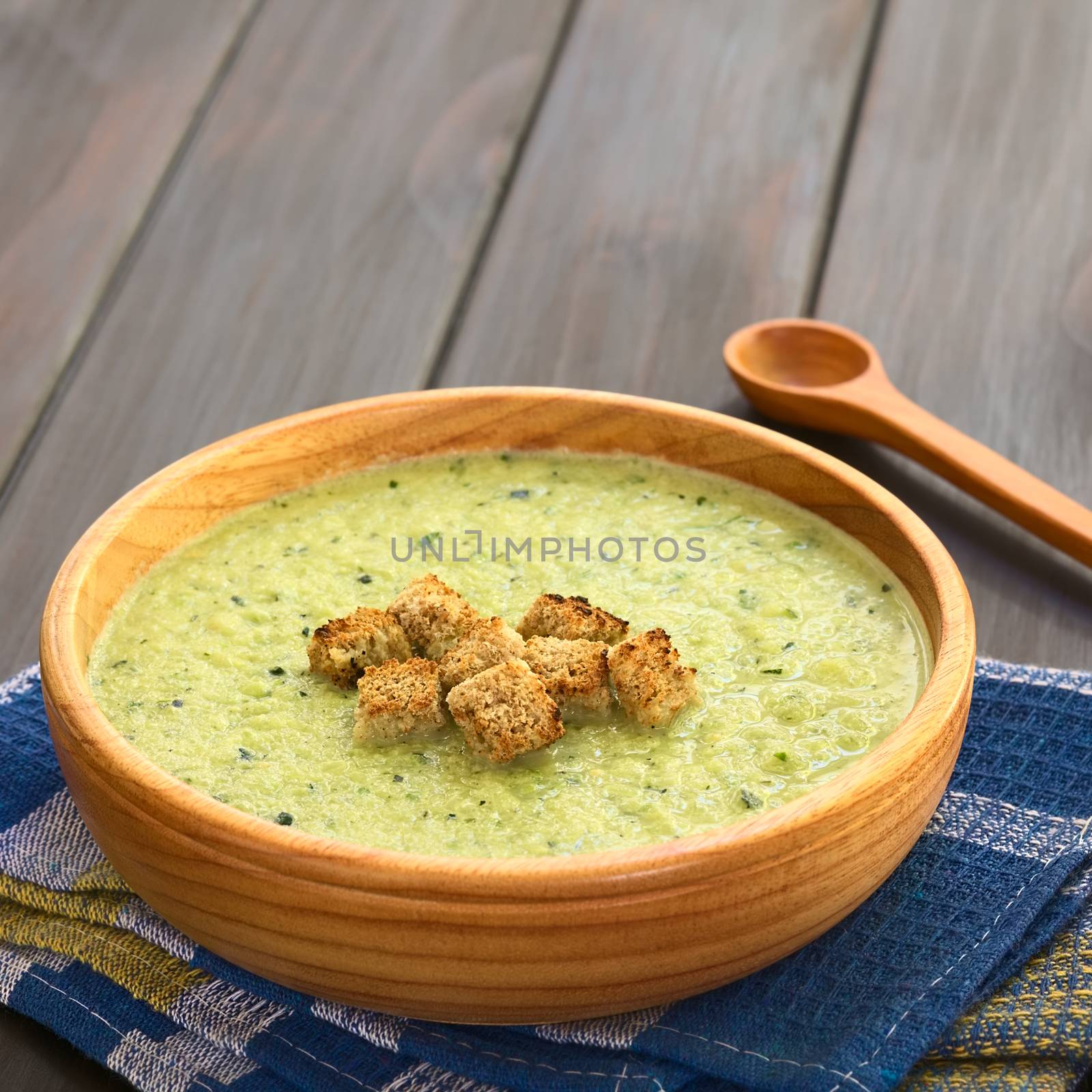 Cream of zucchini soup in wooden bowl with homemade croutons on top, photographed with natural light (Selective Focus, Focus on the first croutons)