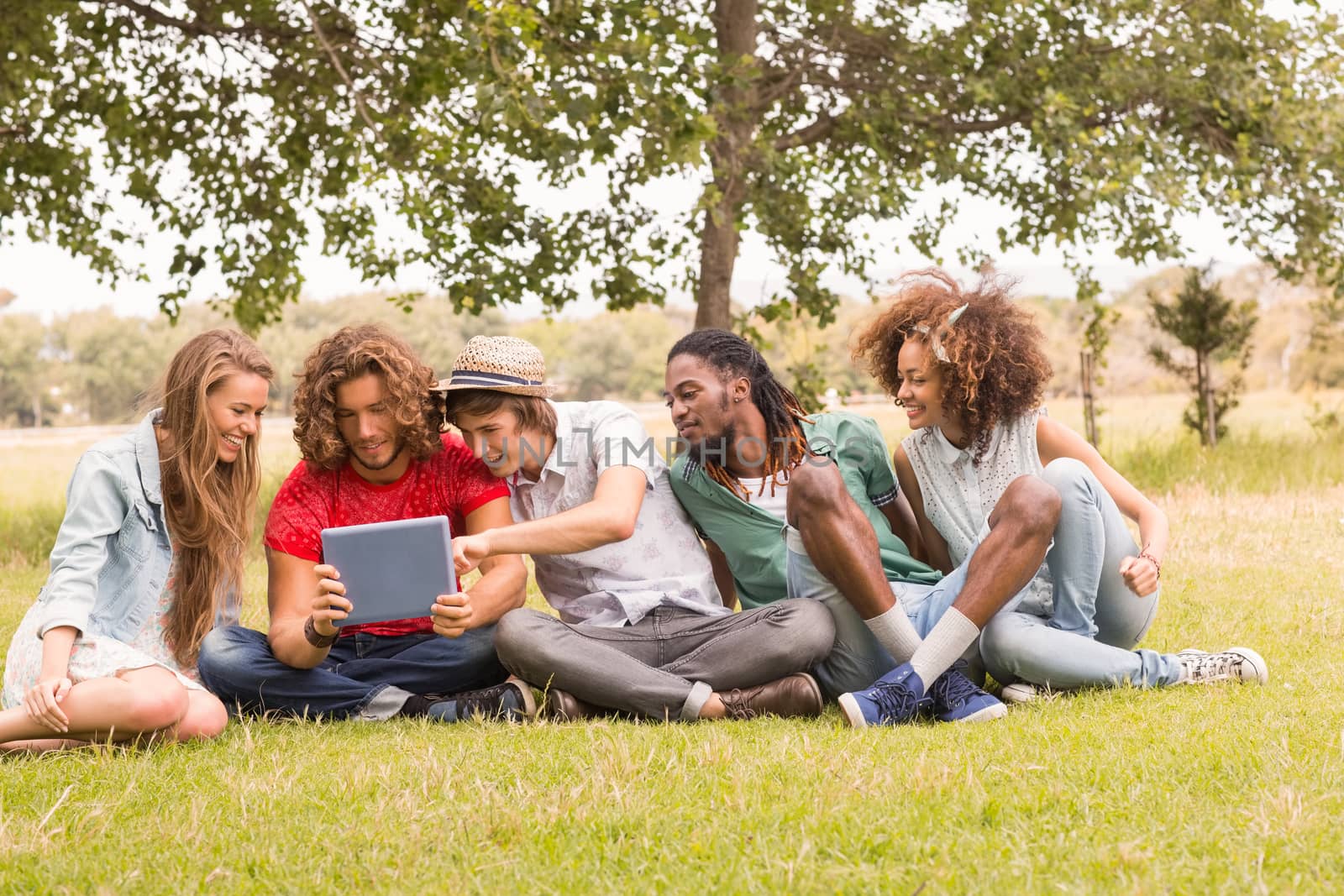 Happy friends in the park looking at tablet by Wavebreakmedia