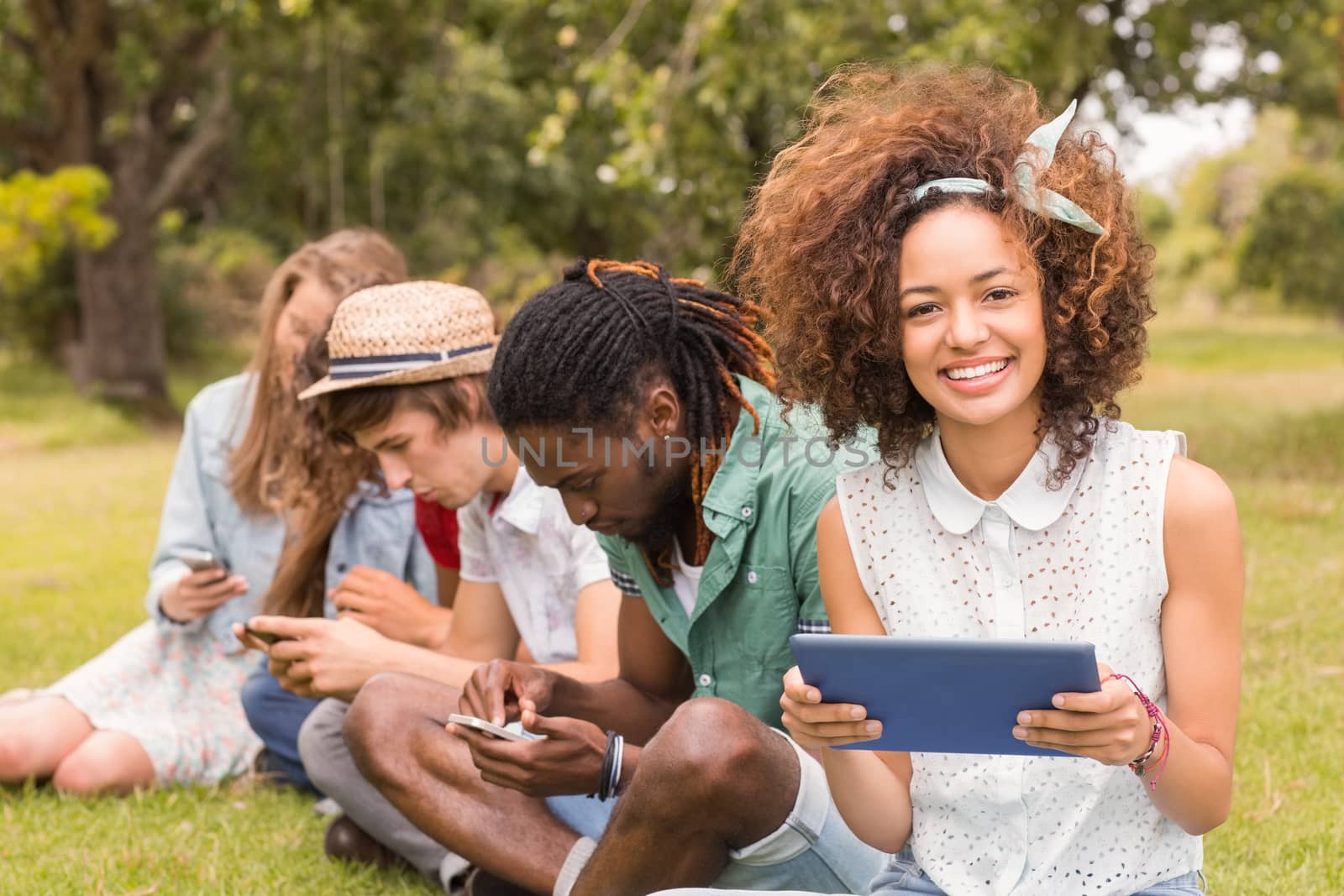 Happy friends in the park looking at tablet on a sunny day