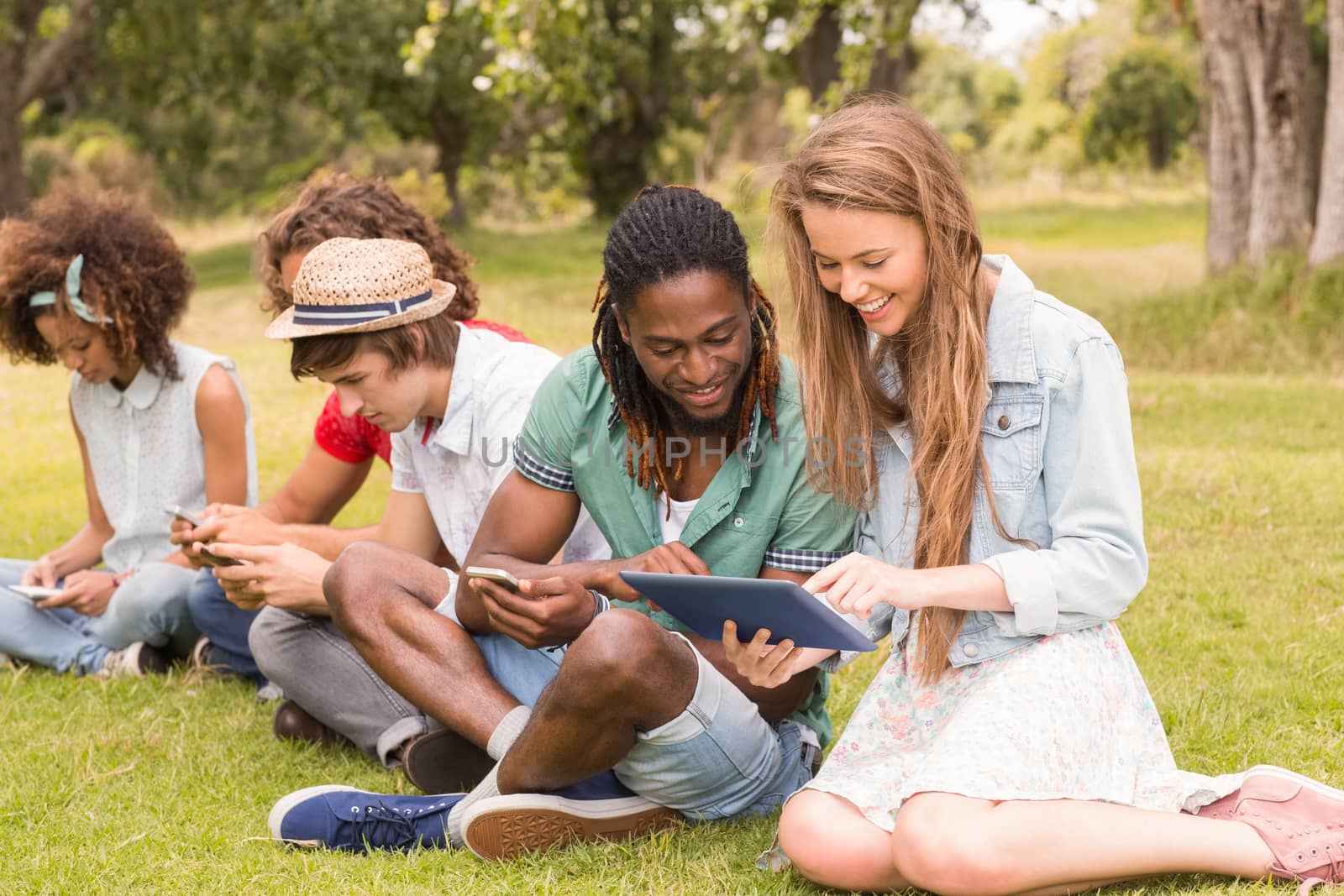 Happy friends in the park looking at tablet by Wavebreakmedia