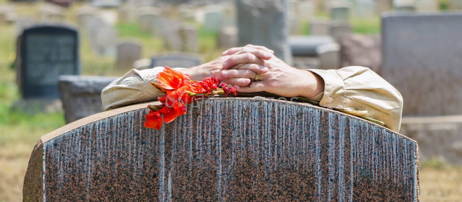 Lone figure of person's hands grieving at cemetery