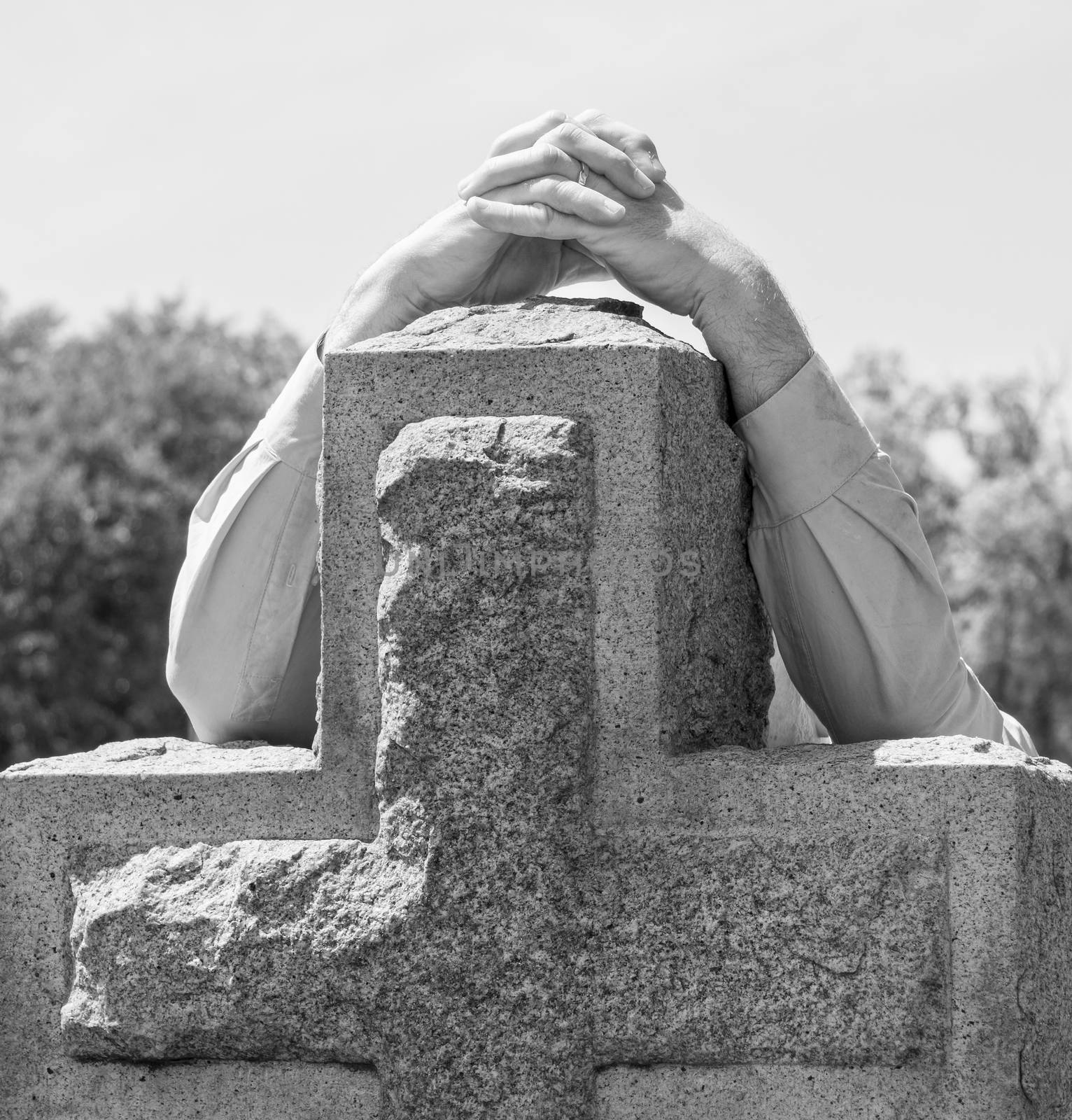 Black and white lone figure of person's hands grieving at cemetery