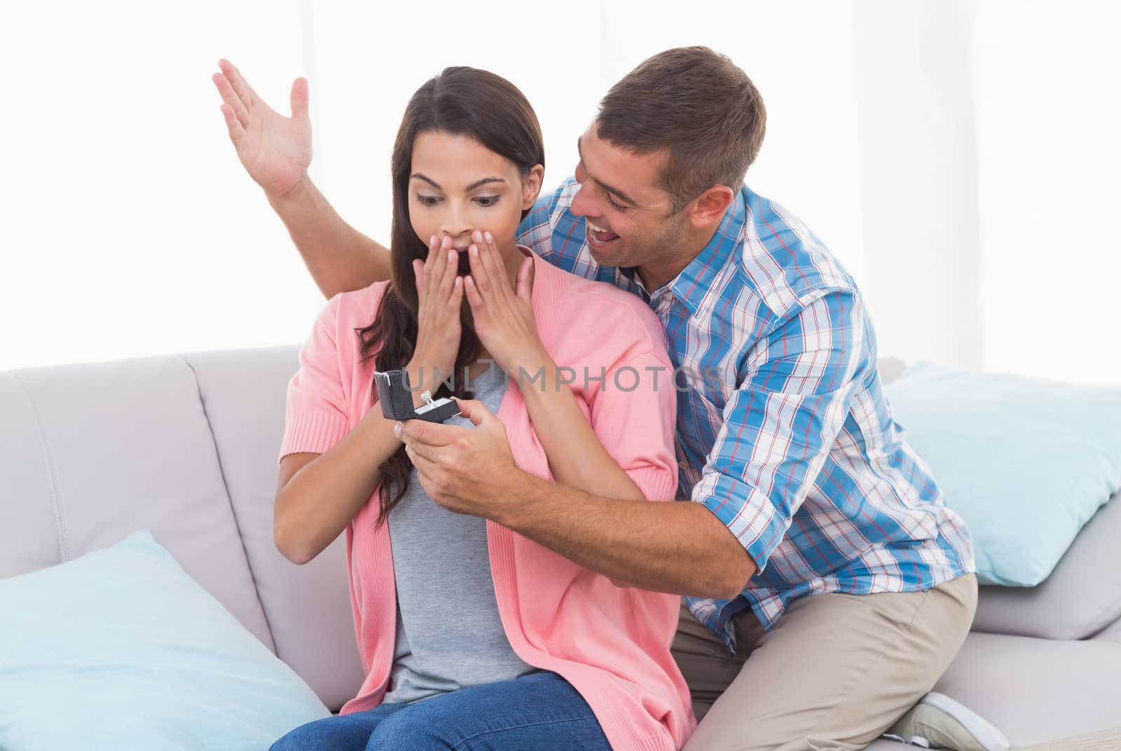 Man gifting ring to surprised woman on sofa by Wavebreakmedia