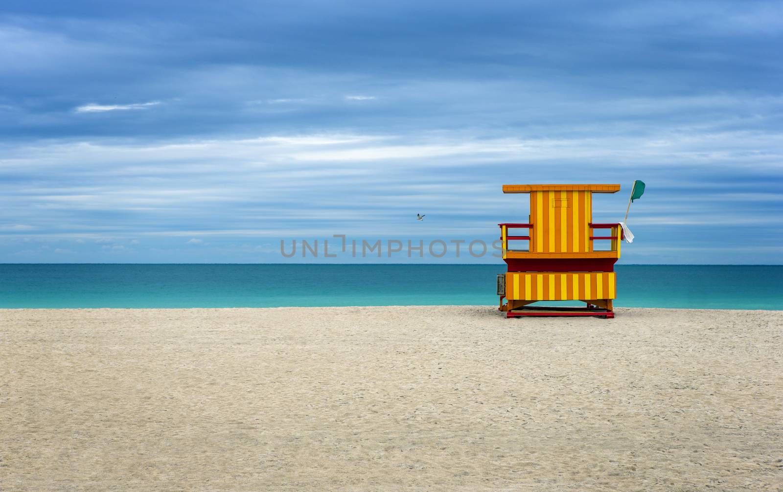 Colorful Life Guard house on an empty beach, cloudy blue sky.