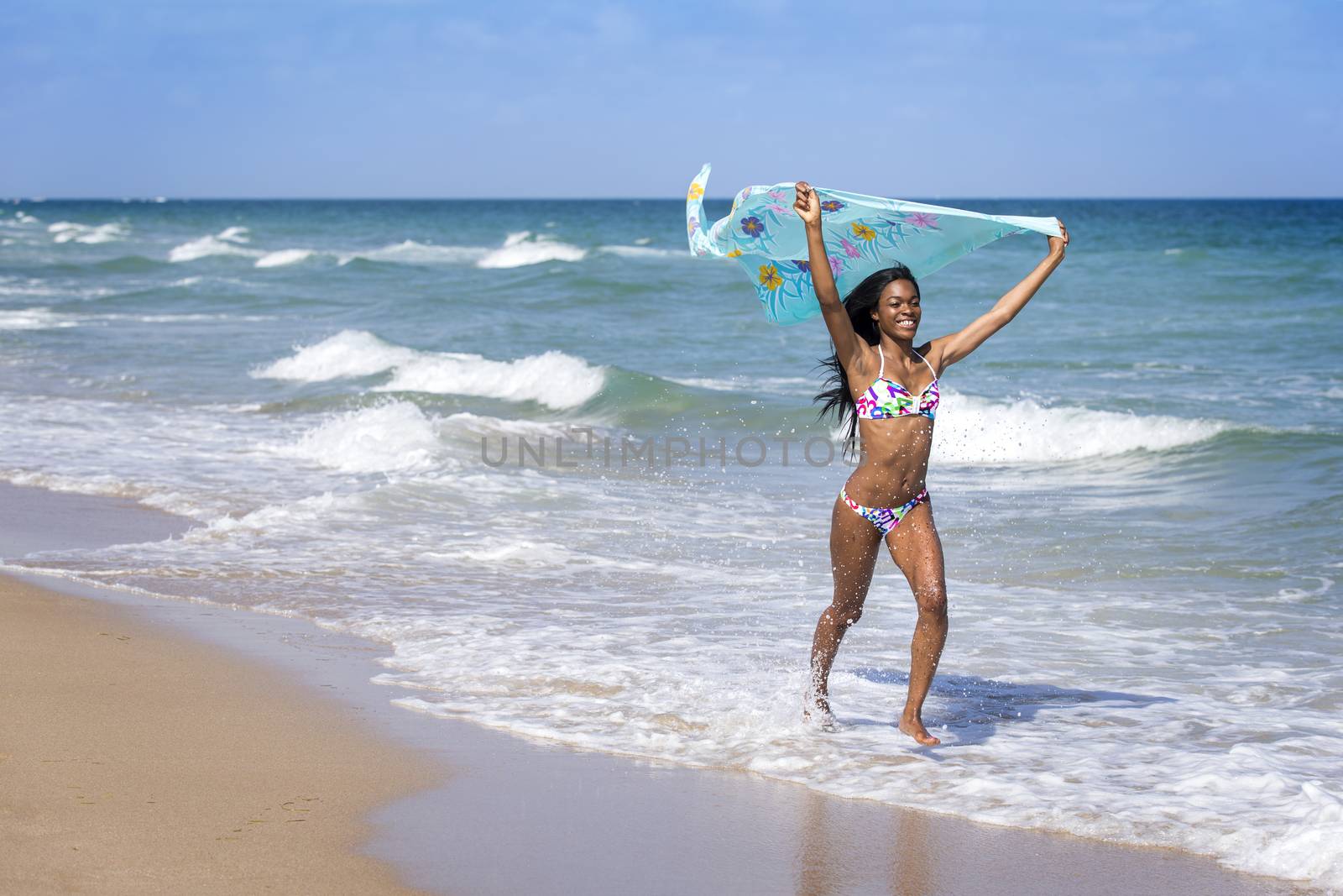 Young woman walking on the beach with a colored sarong by BrazilPhoto